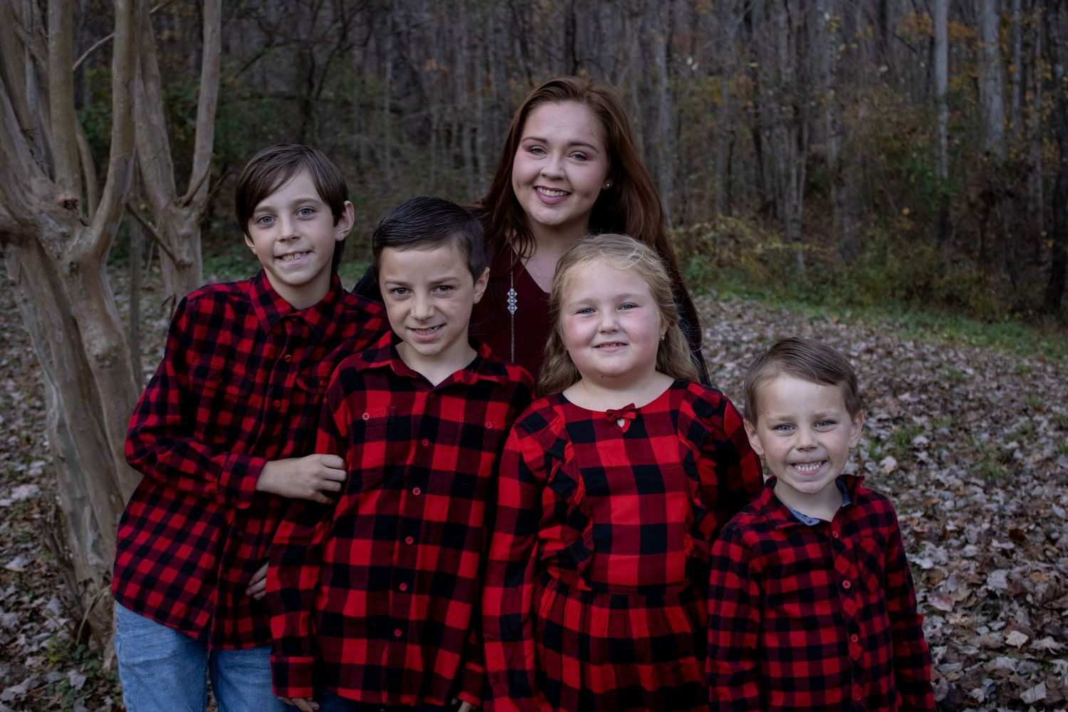 A group wearing matching buffalo plaid flannel shirts poses in a wooded setting.