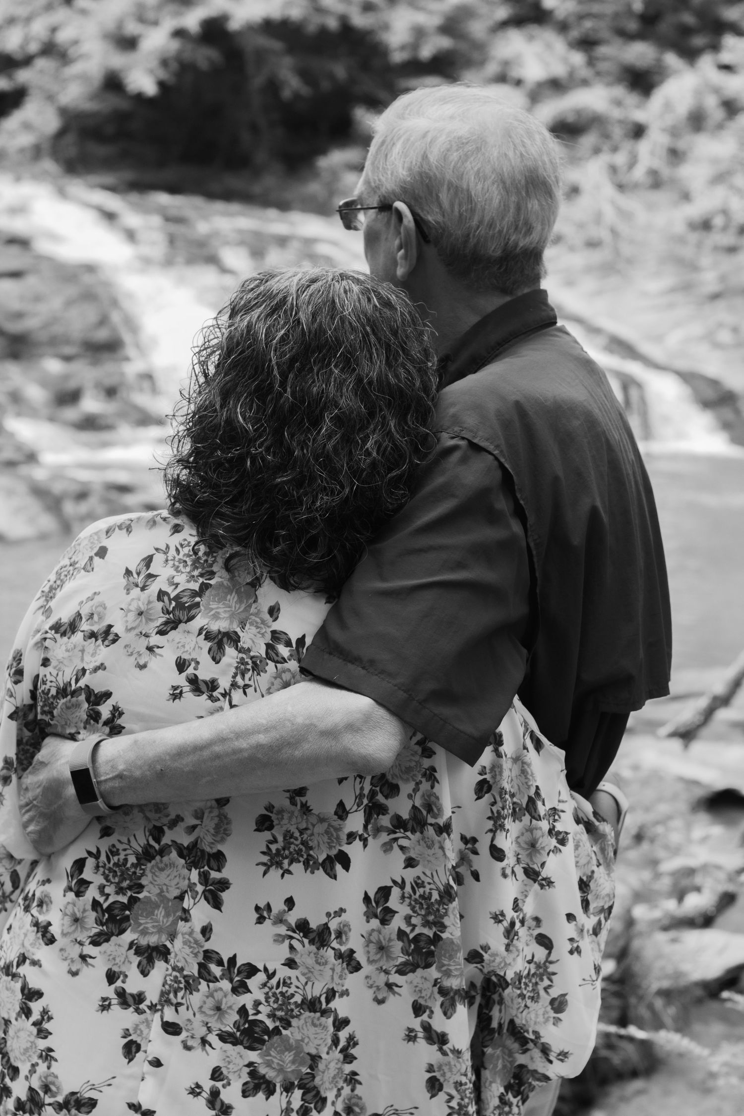 Couple in casual wear sitting close together near a scenic overlook.