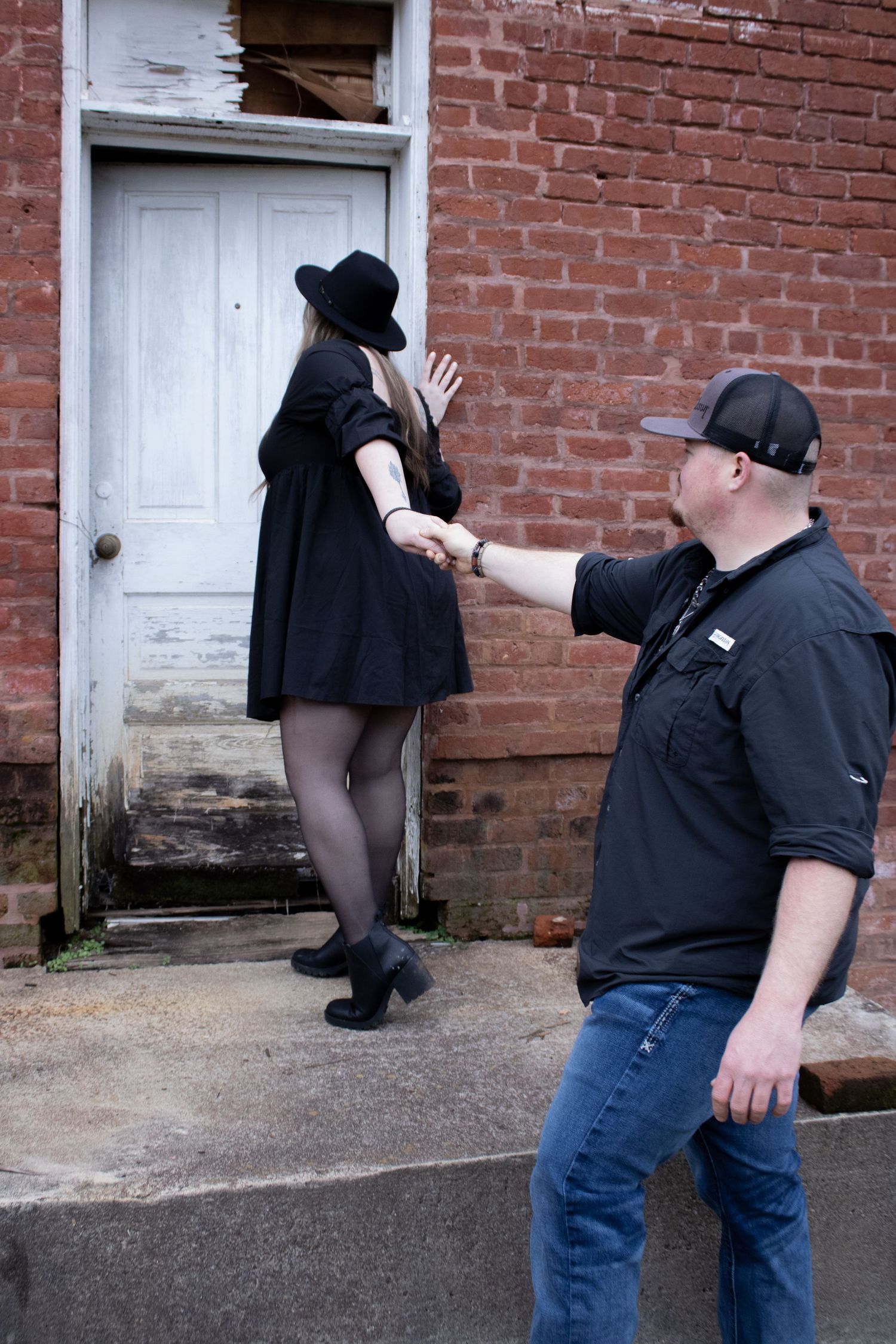 Couple in black and denim sharing playful moments by brick building.