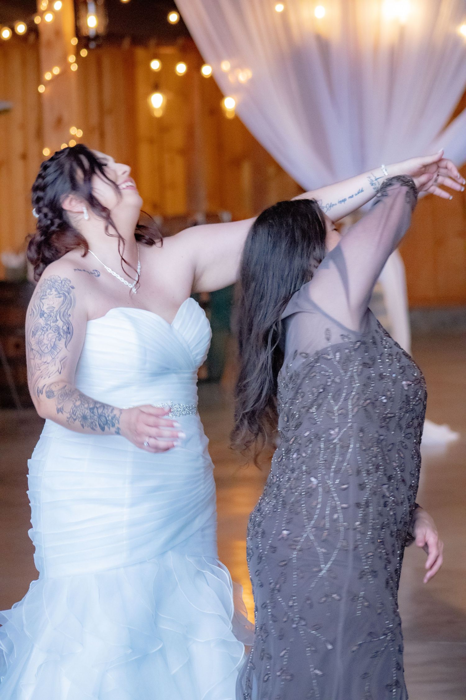 Two people dancing joyfully in an indoor venue with string lights and white decor.
