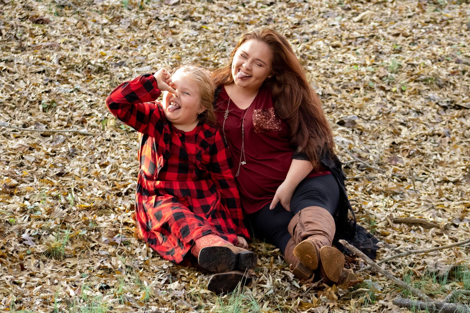 Two people in red clothing share a laugh while sitting on ground covered in autumn leaves.