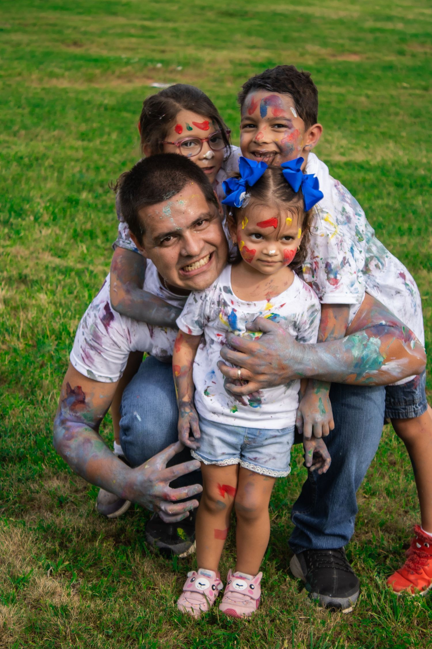 Candid moments of paint-covered family playing together in a grassy field.