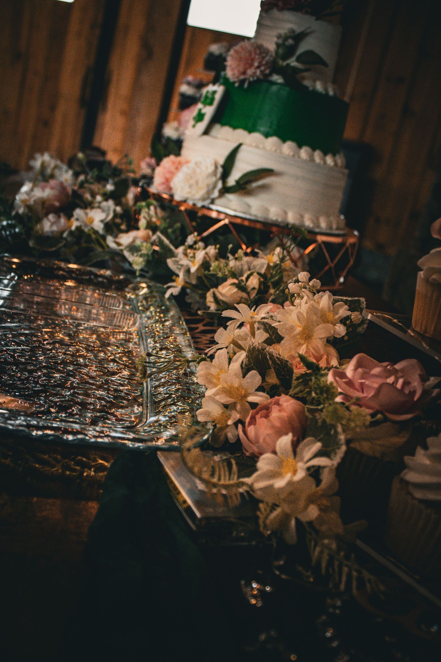 Elegant wedding cake with green ribbon detail surrounded by delicate floral arrangements on a rustic wooden table.