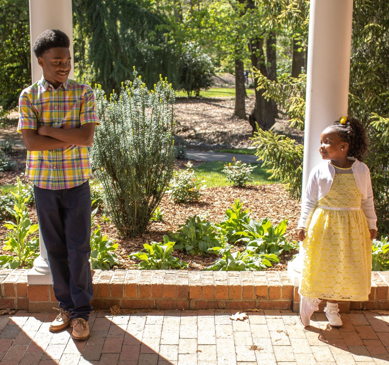 Two people stand on a brick patio with garden plants and columns in the background.