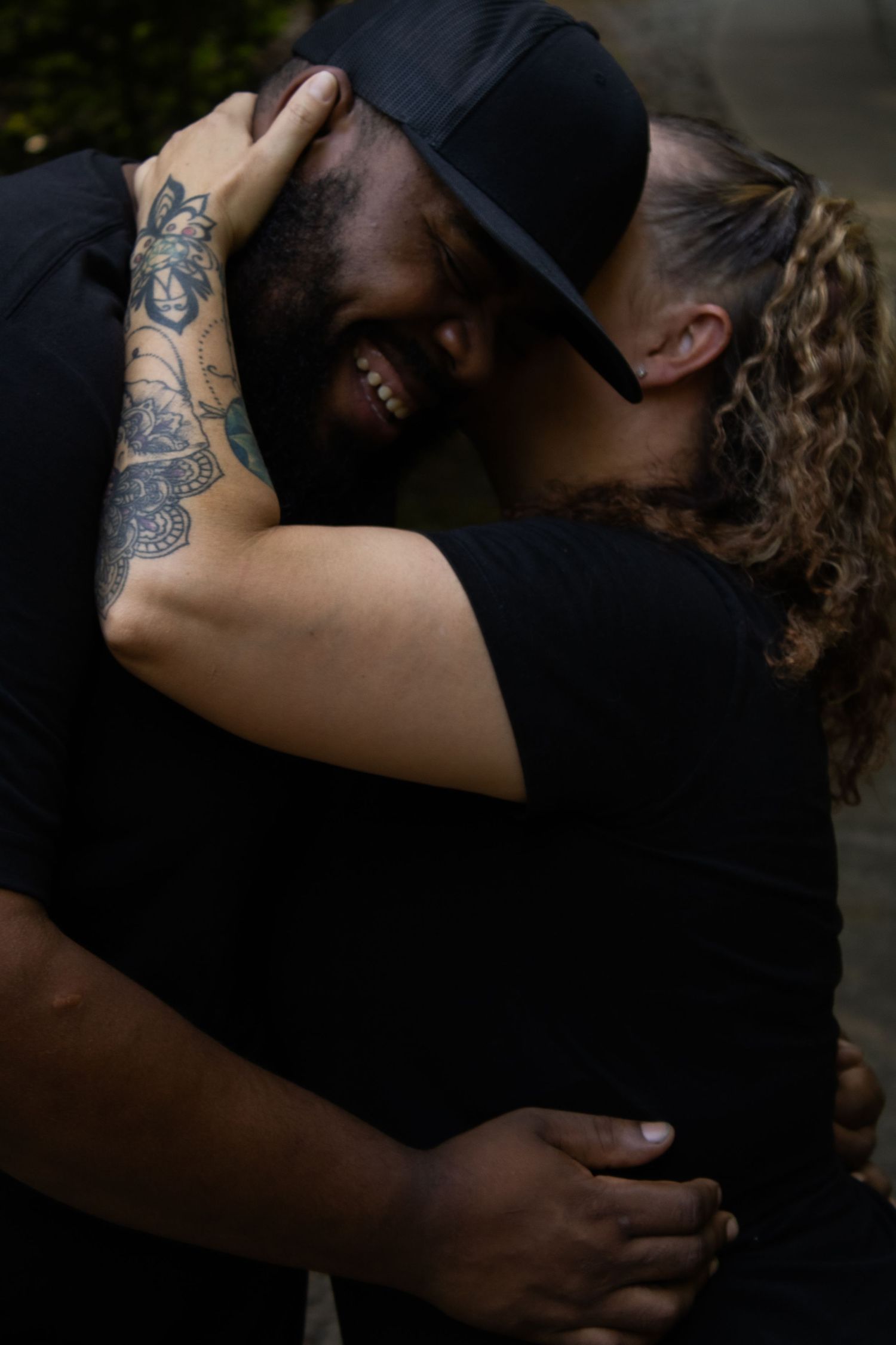 An intimate embrace between two people with visible tattoos in a natural outdoor setting.