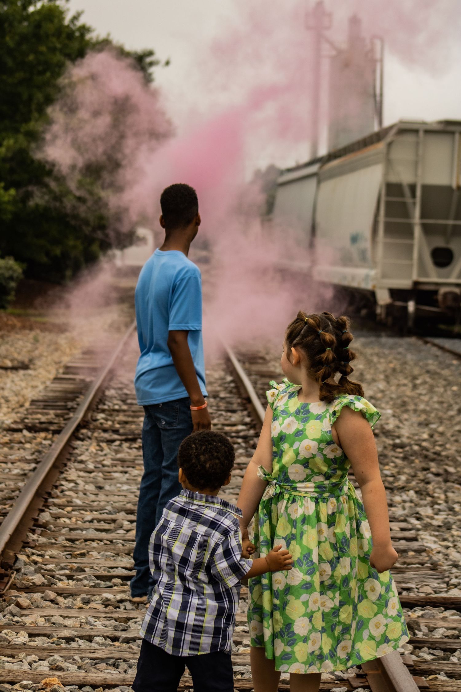 People standing on train tracks with pink smoke in background wearing casual attire.