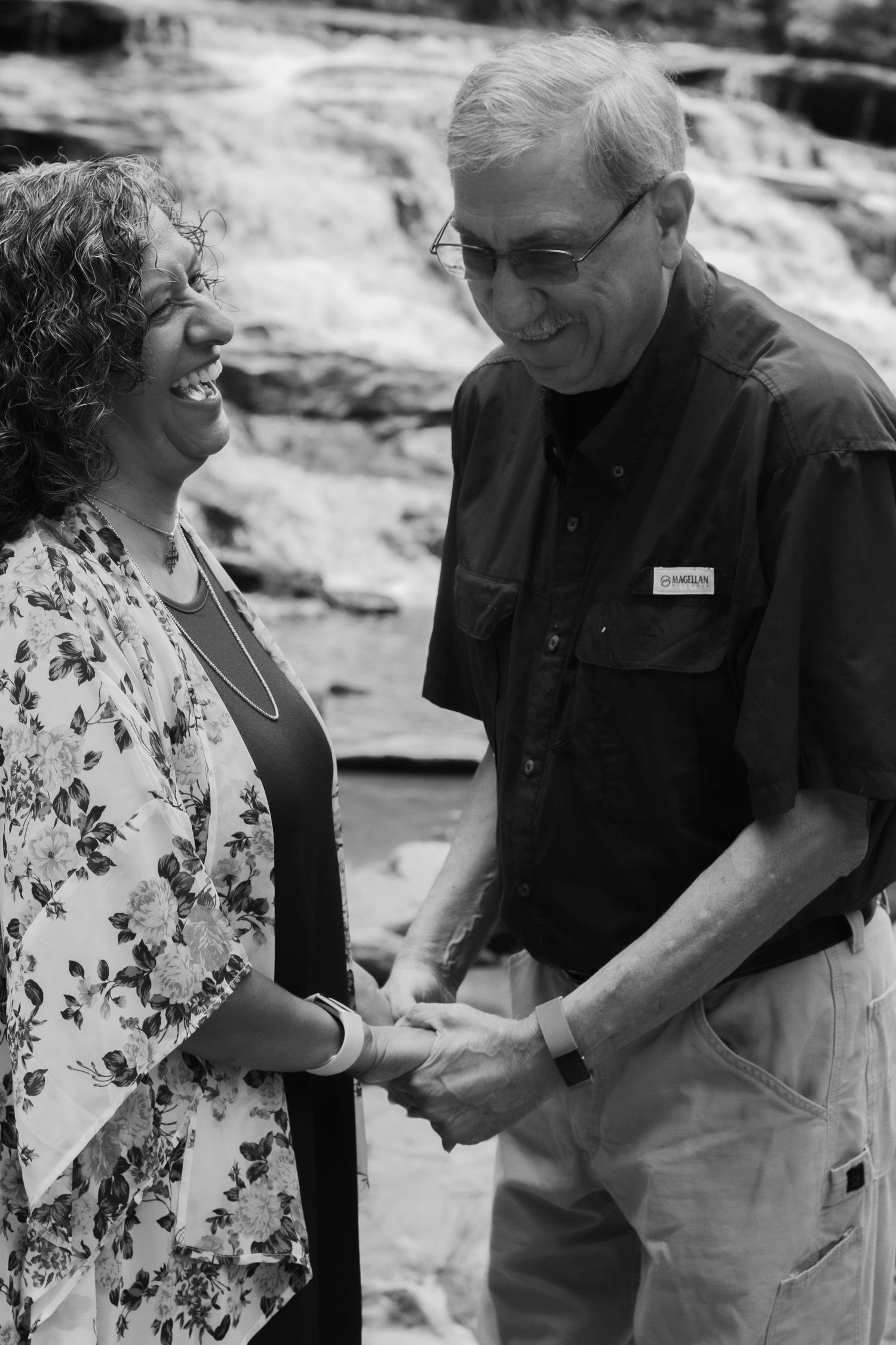 A black and white photo of two people sharing a moment outdoors near rocky terrain.