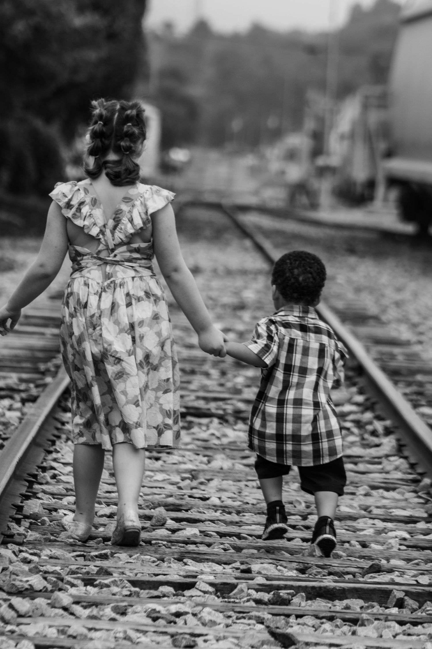 Black and white photo of two people walking along railroad tracks holding hands.