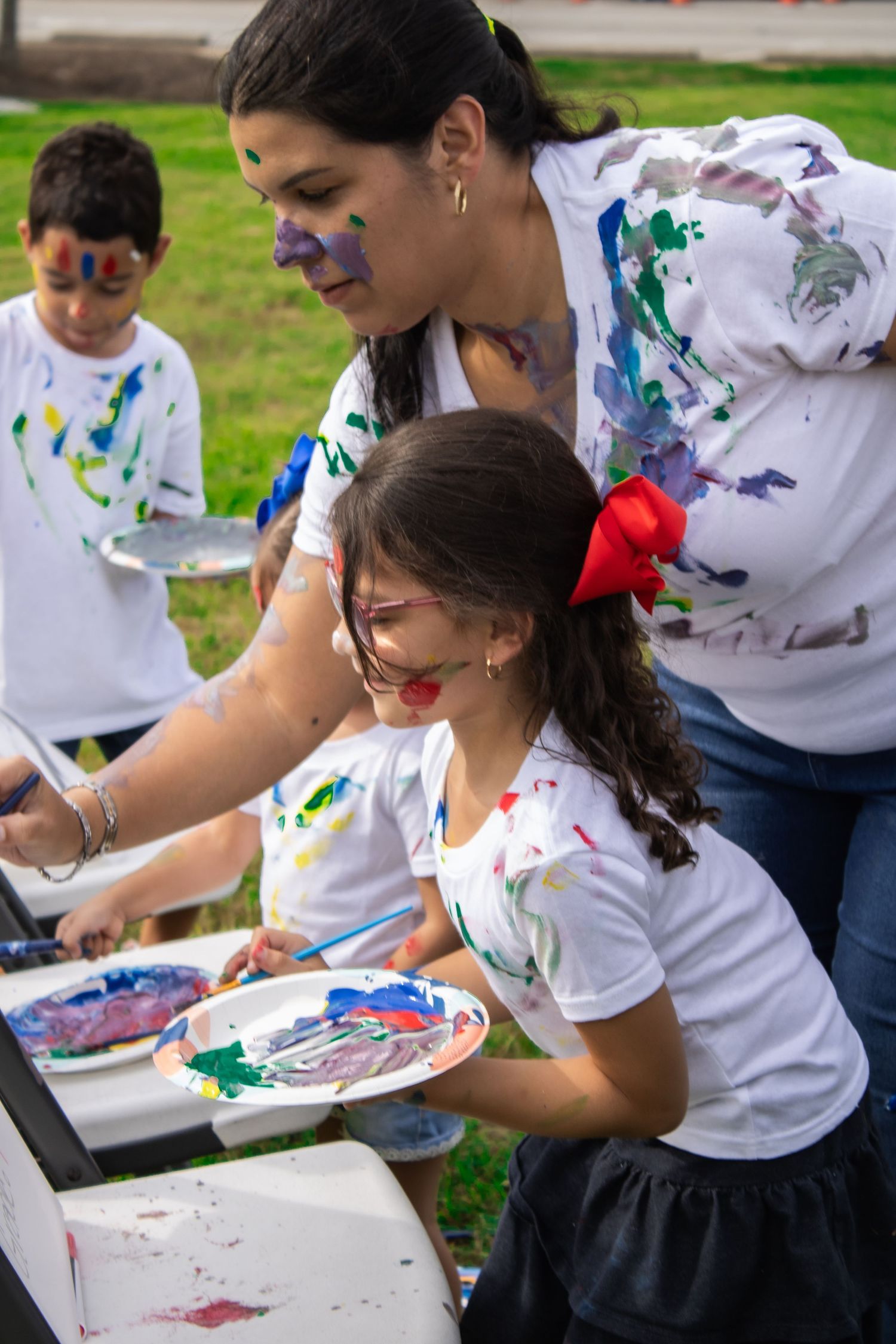 People in paint-splattered white shirts work on art projects outdoors.