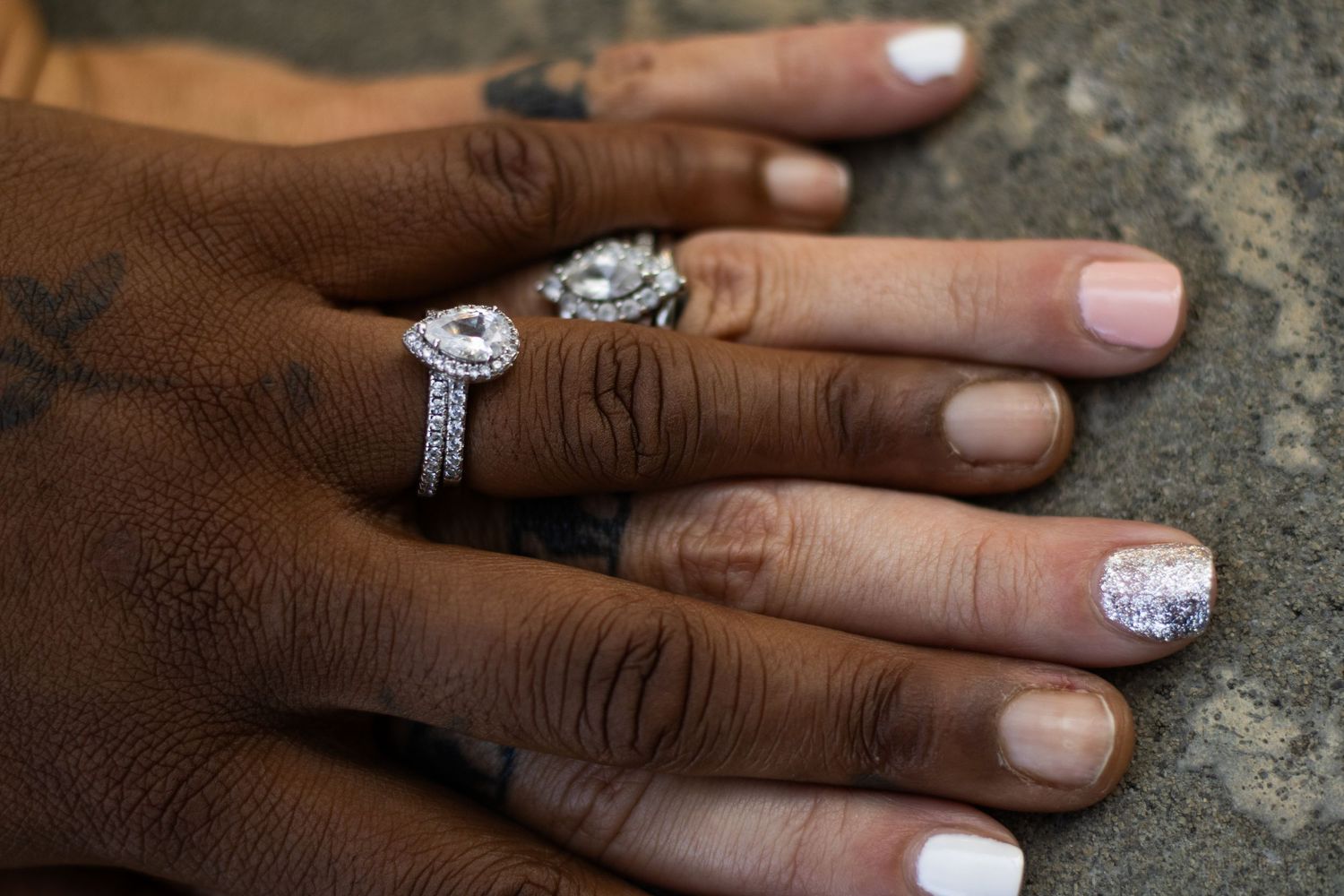Close-up of hands with engagement rings and white nail polish showing special moment.