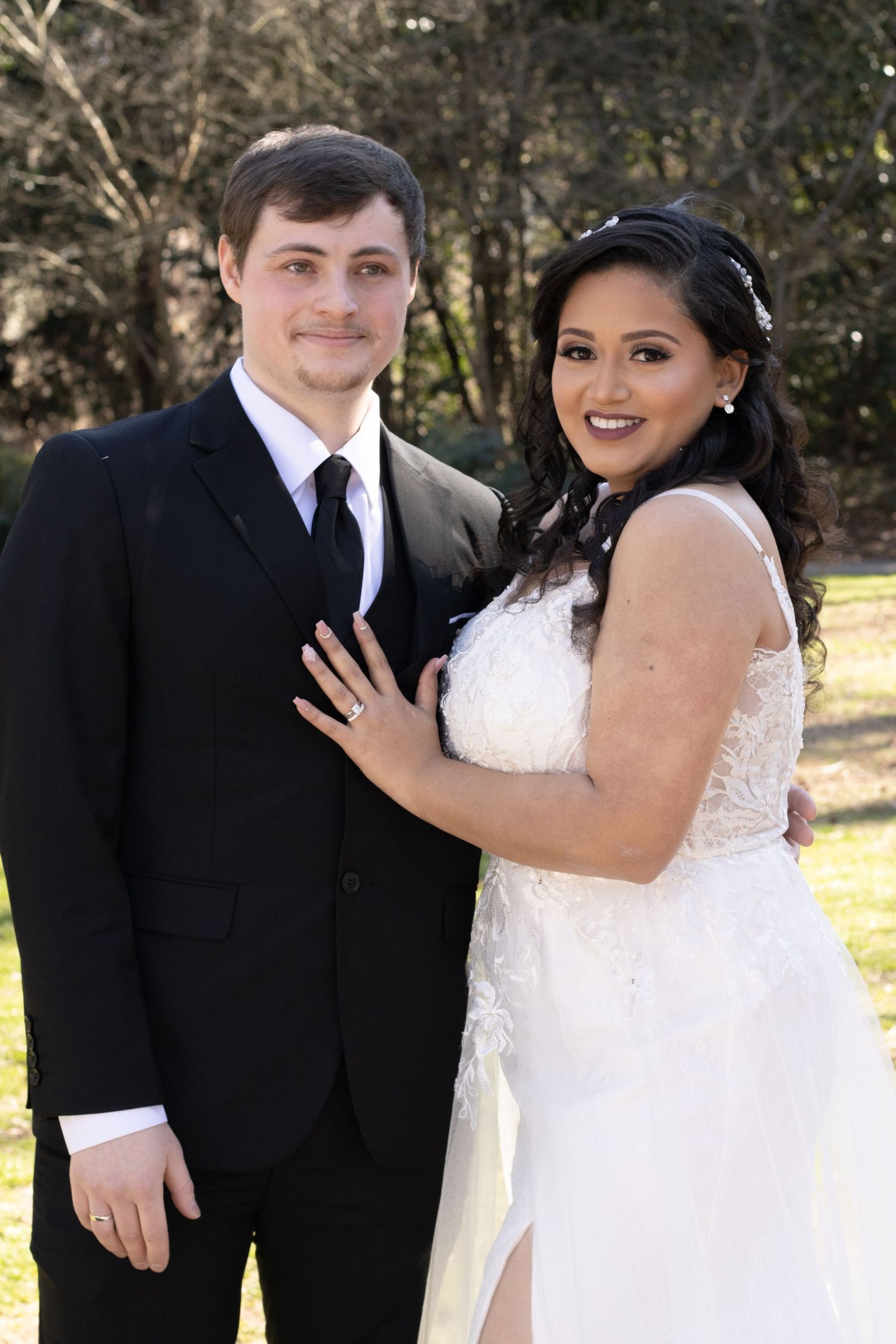 A beautiful outdoor wedding portrait of a couple, the groom in black suit and the bride in a white lace dress.