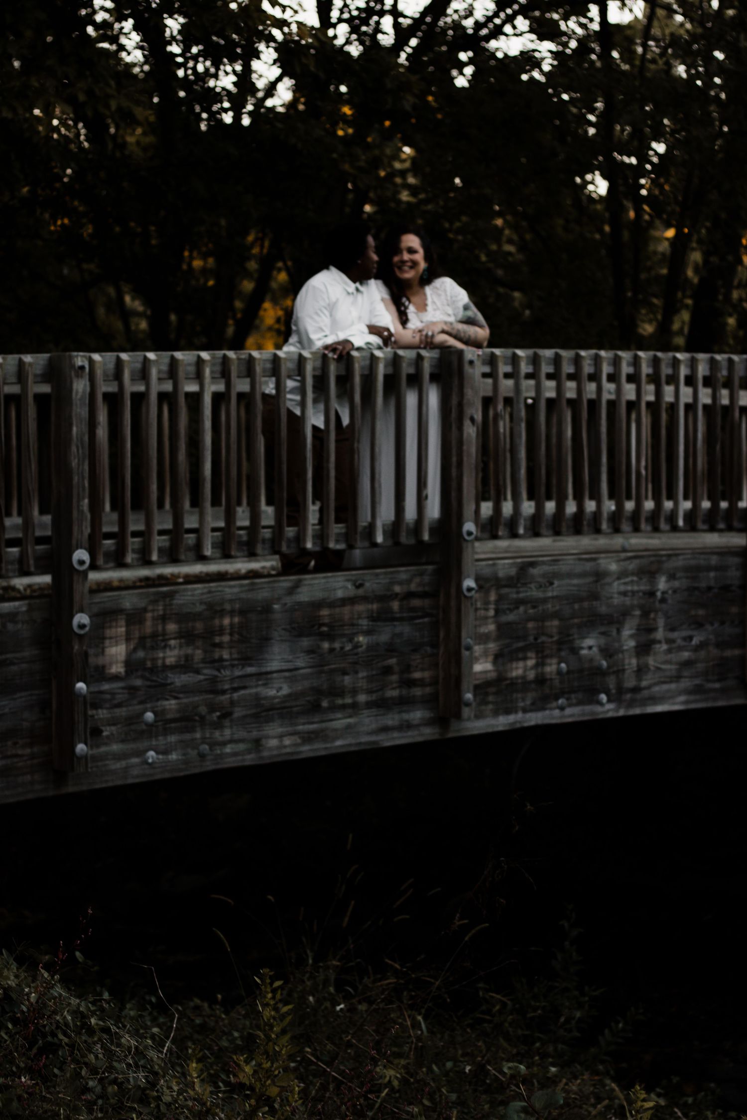 A couple in white outfits share an intimate moment on a wooden bridge at sunset.