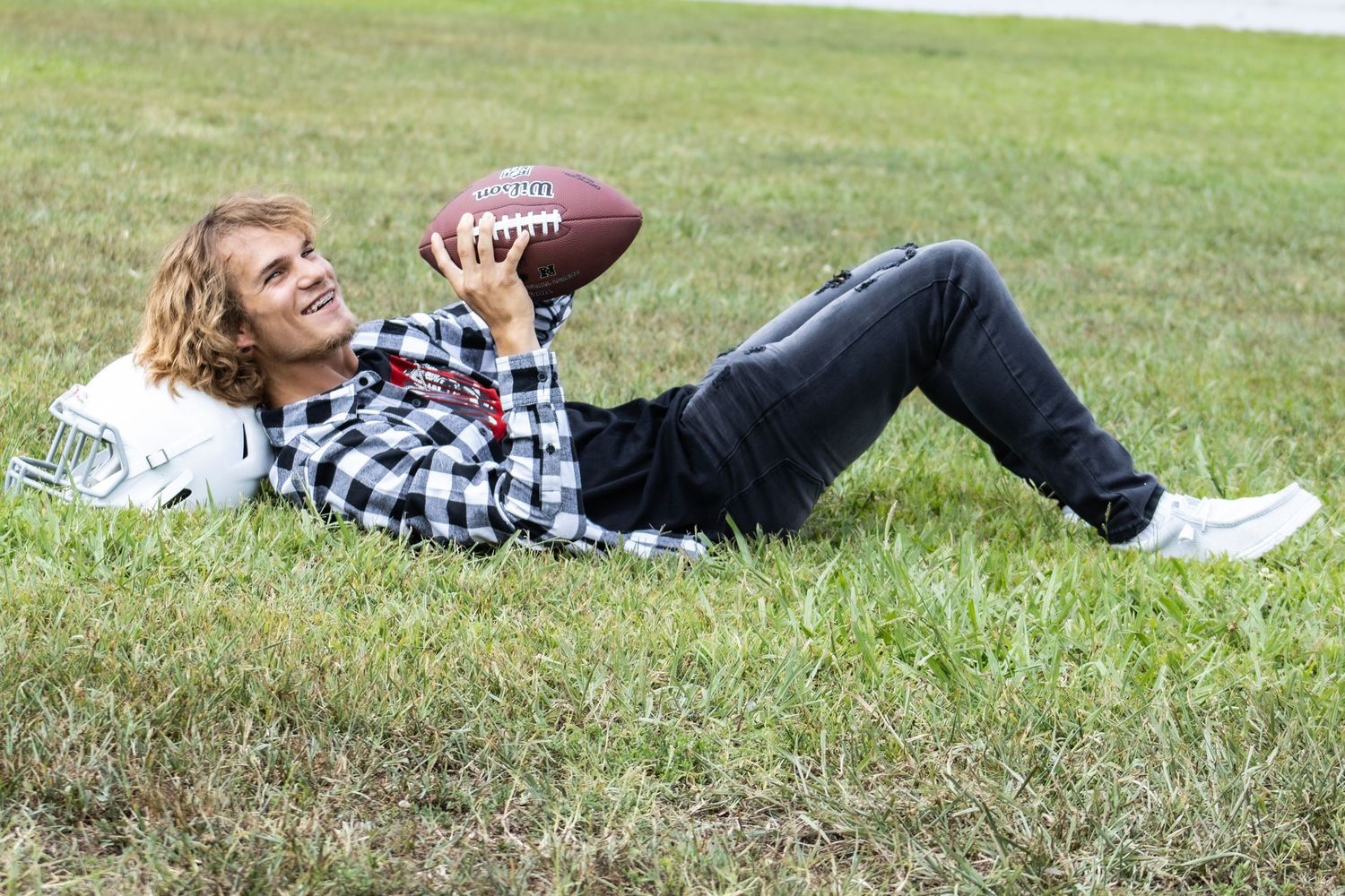 A player in plaid shirt lies on grass holding a football.