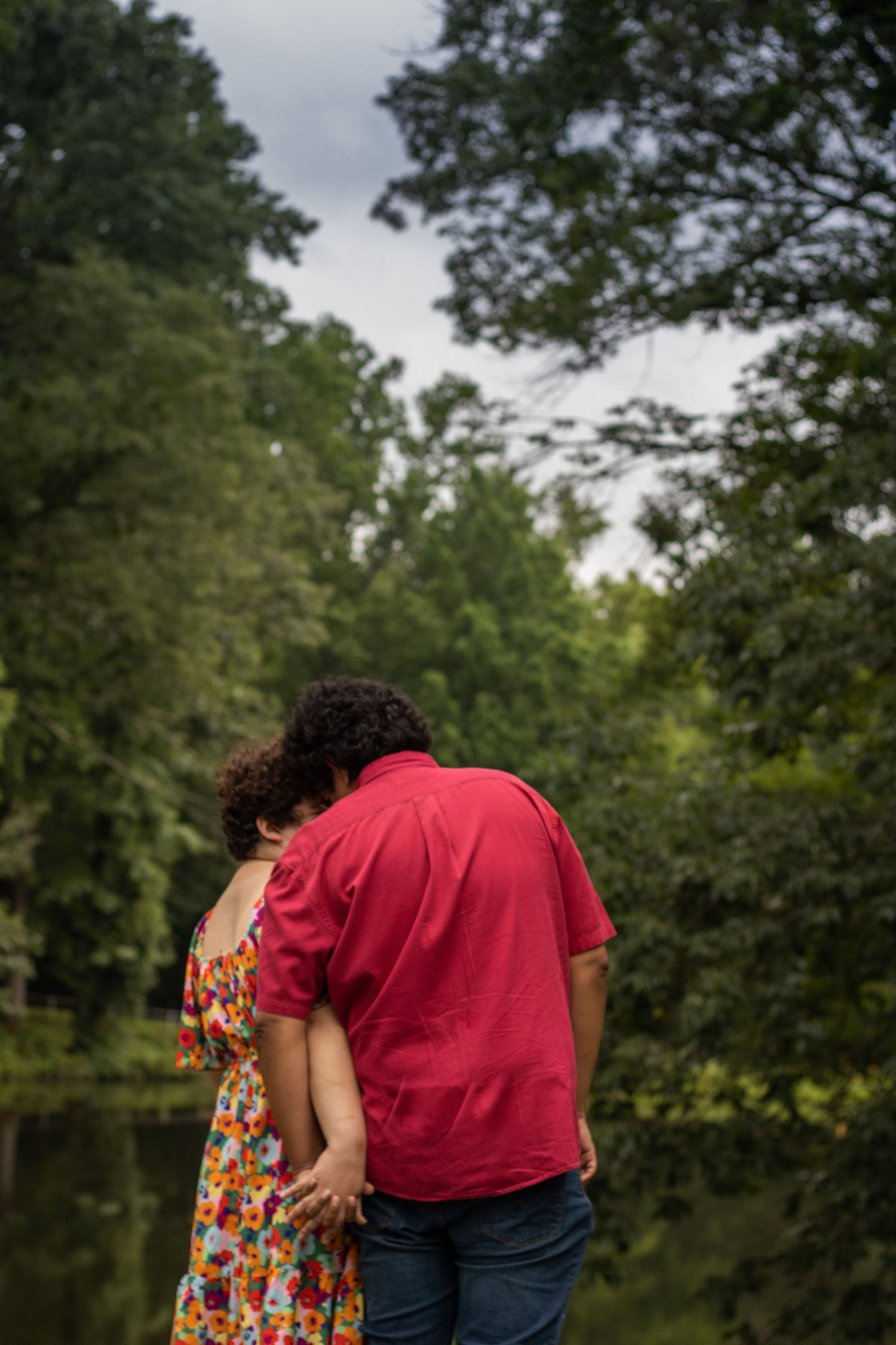 A couple stands close together against a scenic backdrop of trees and nature.