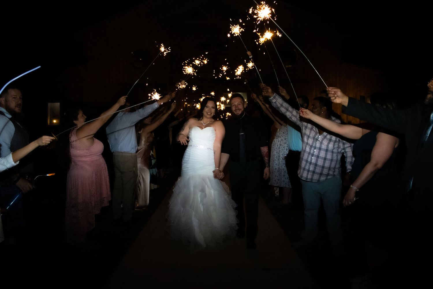 Wedding guests create sparkler tunnel during evening reception celebrations.