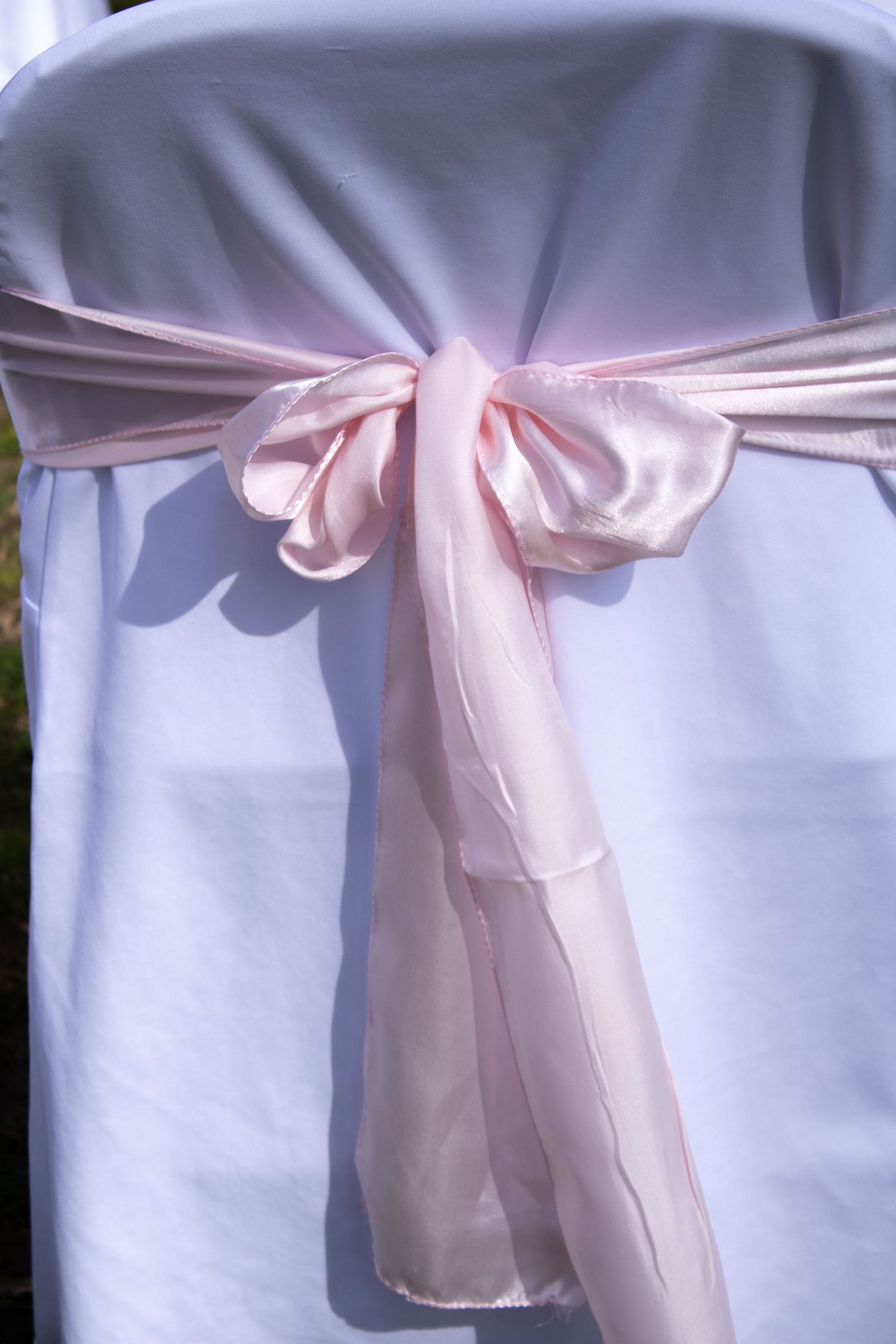 Pink satin bow tied around a white chair cover creating an elegant wedding decoration.