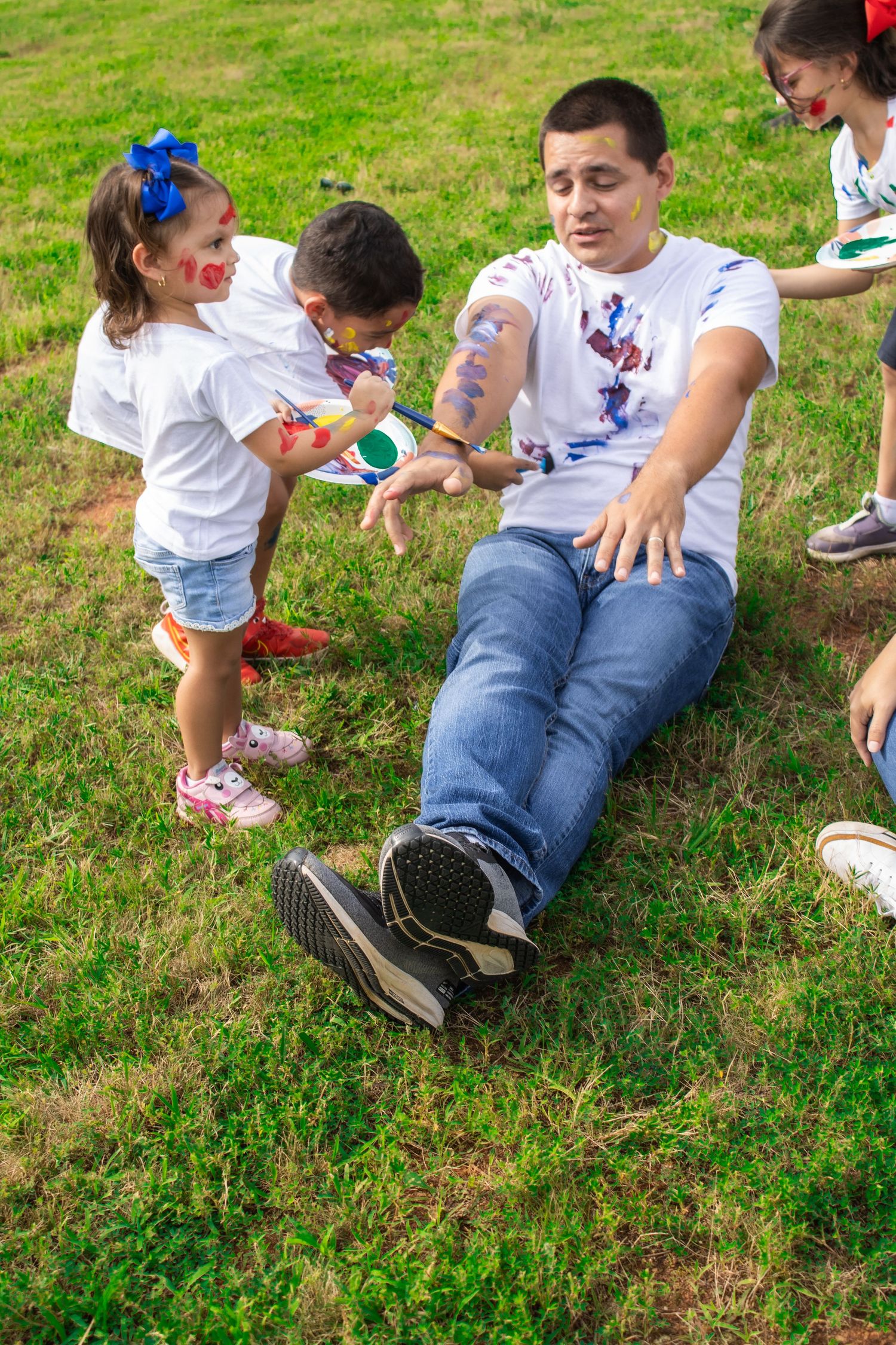 Family members lay in grass showing paint-covered clothes from their fun activity.