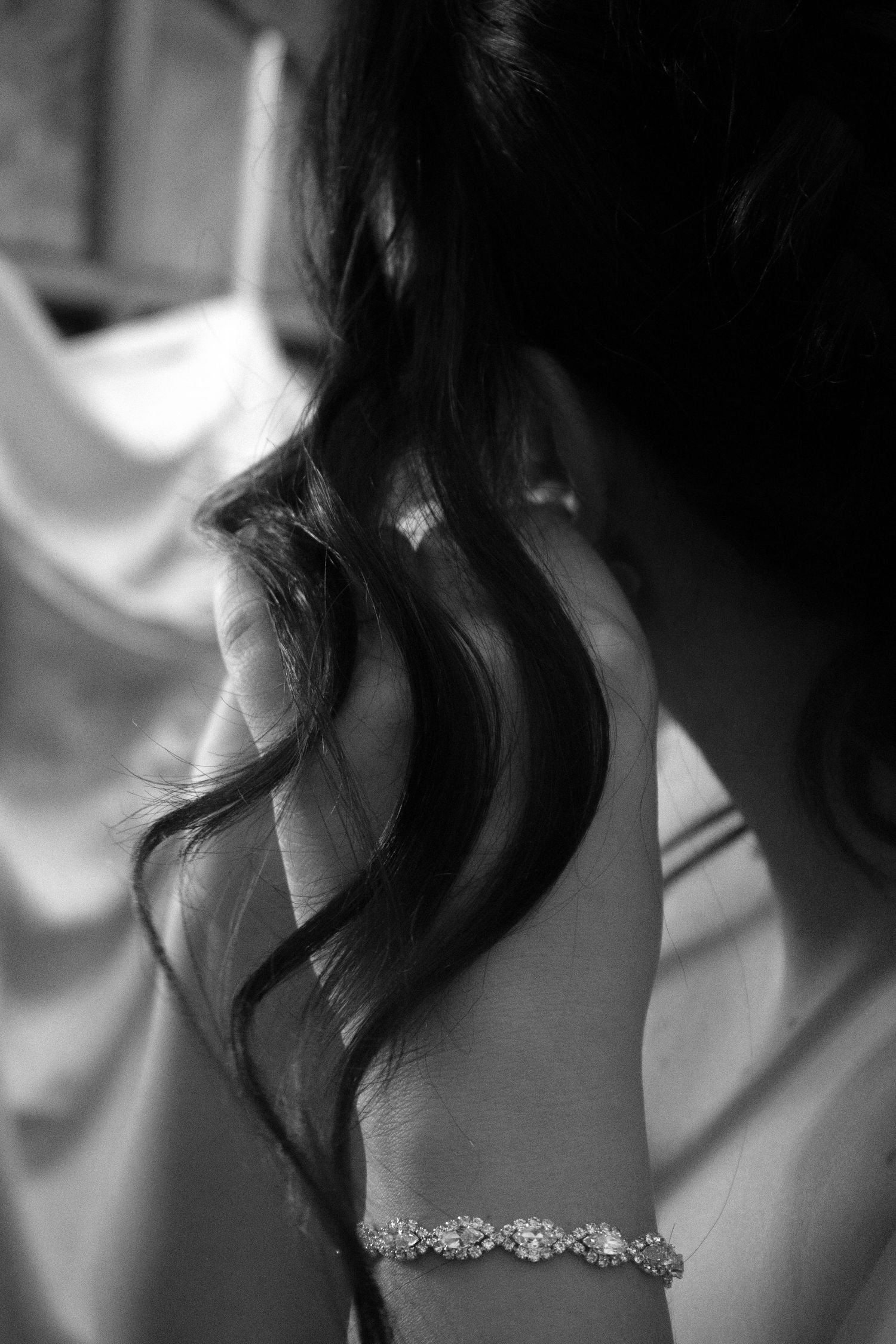 Black and white closeup of elegant bracelet and flowing hair against white fabric.