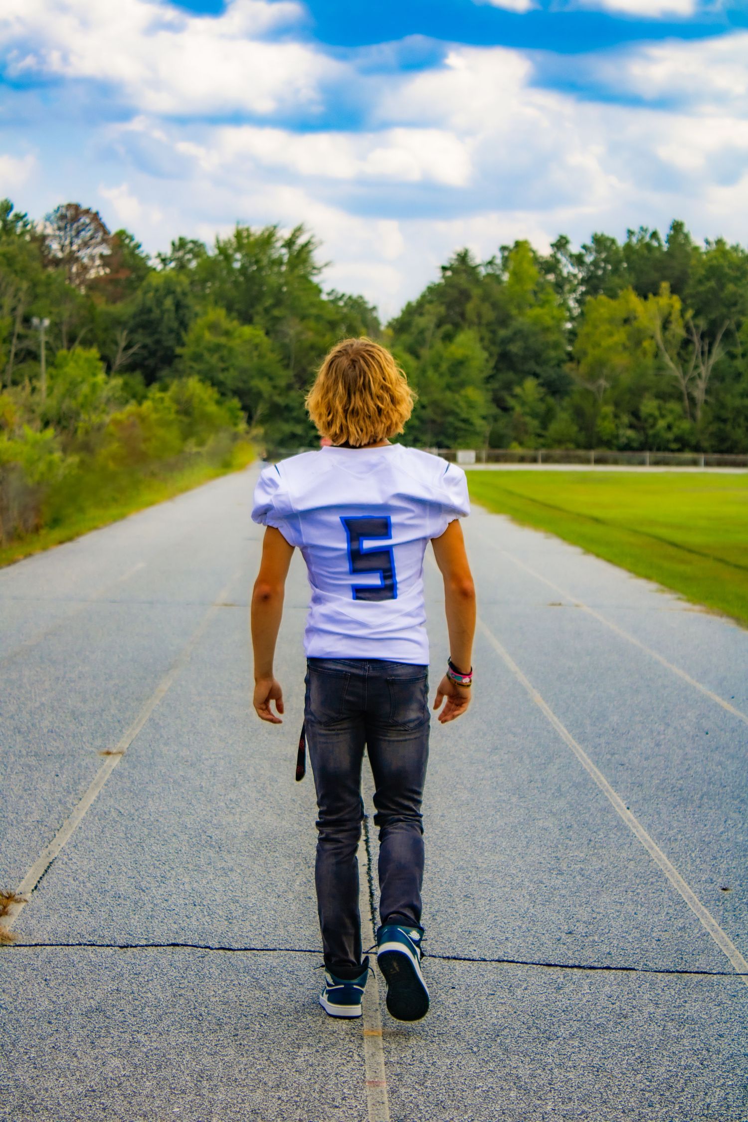 A football player wearing jersey number 5 walks alone on a track under blue skies.