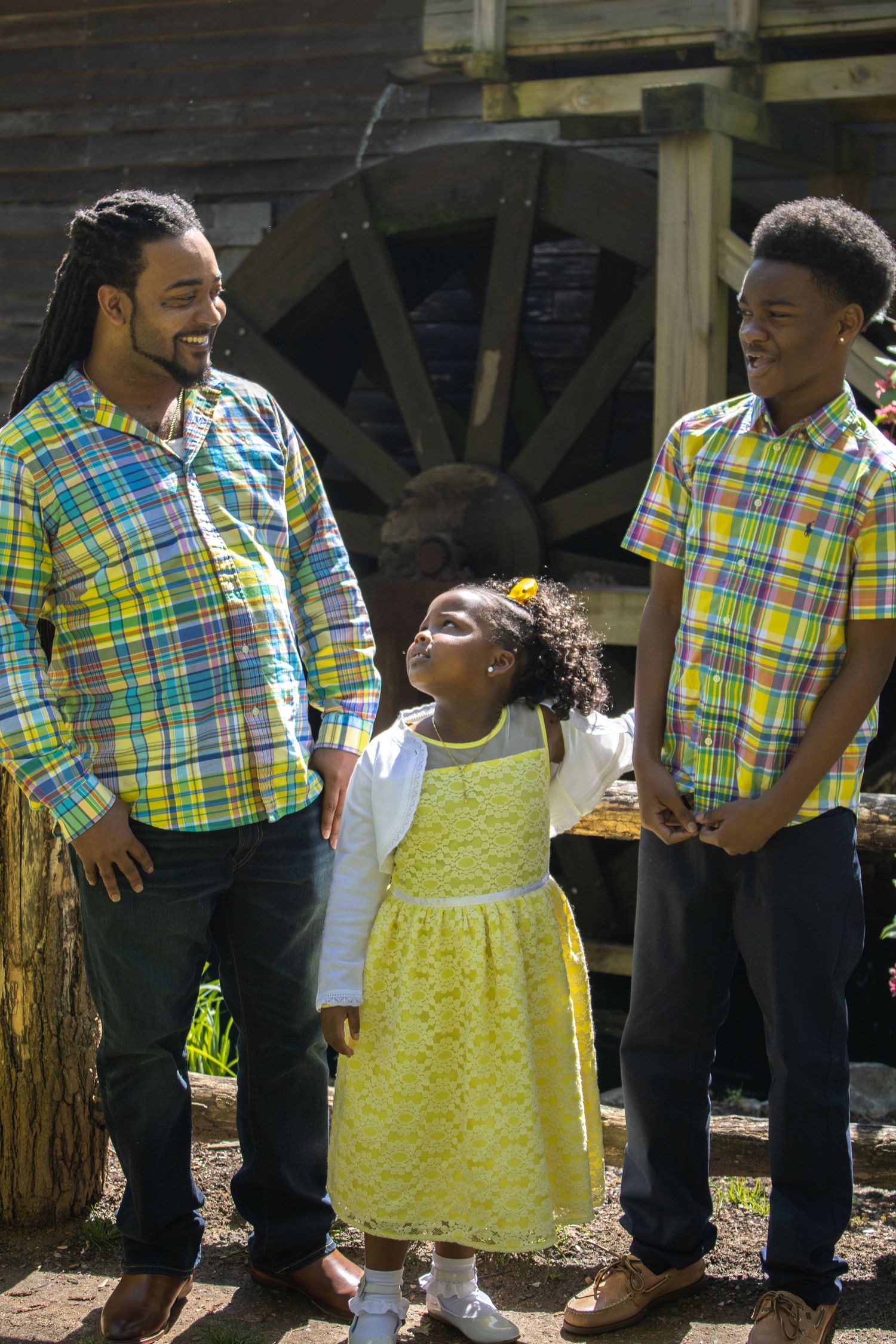 A family in coordinating plaid shirts and yellow dress share a joyful moment together outdoors.