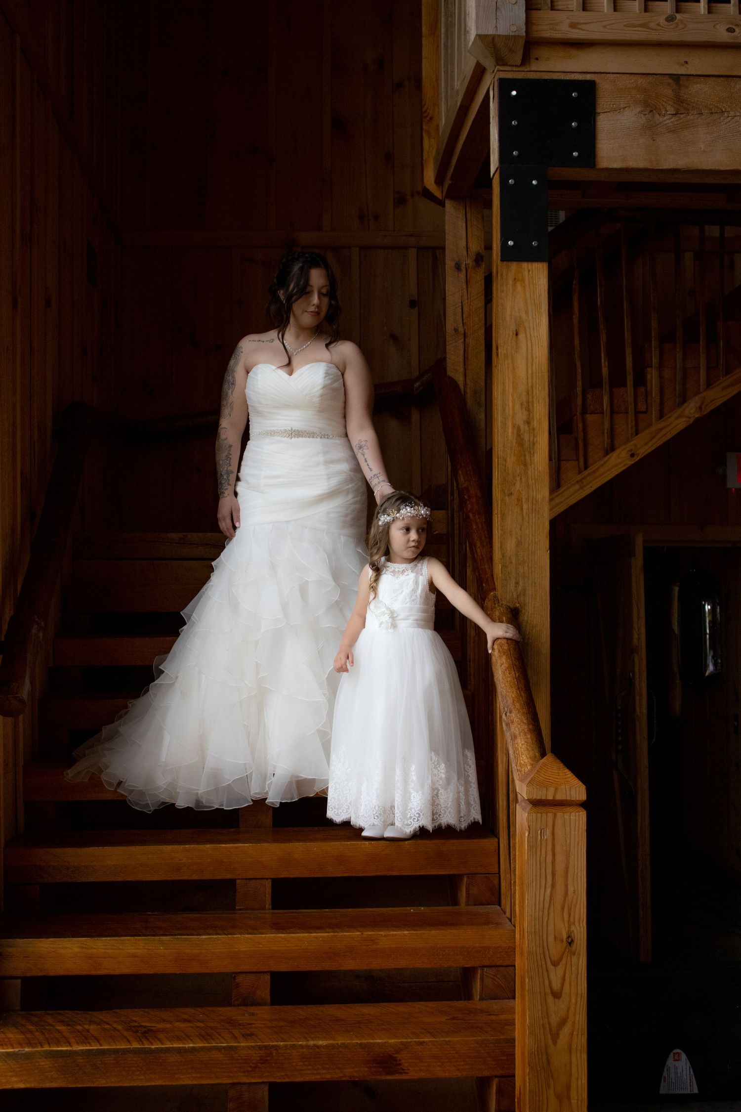 Wedding photo on wooden stairs showing bride and flower girl in white dresses.