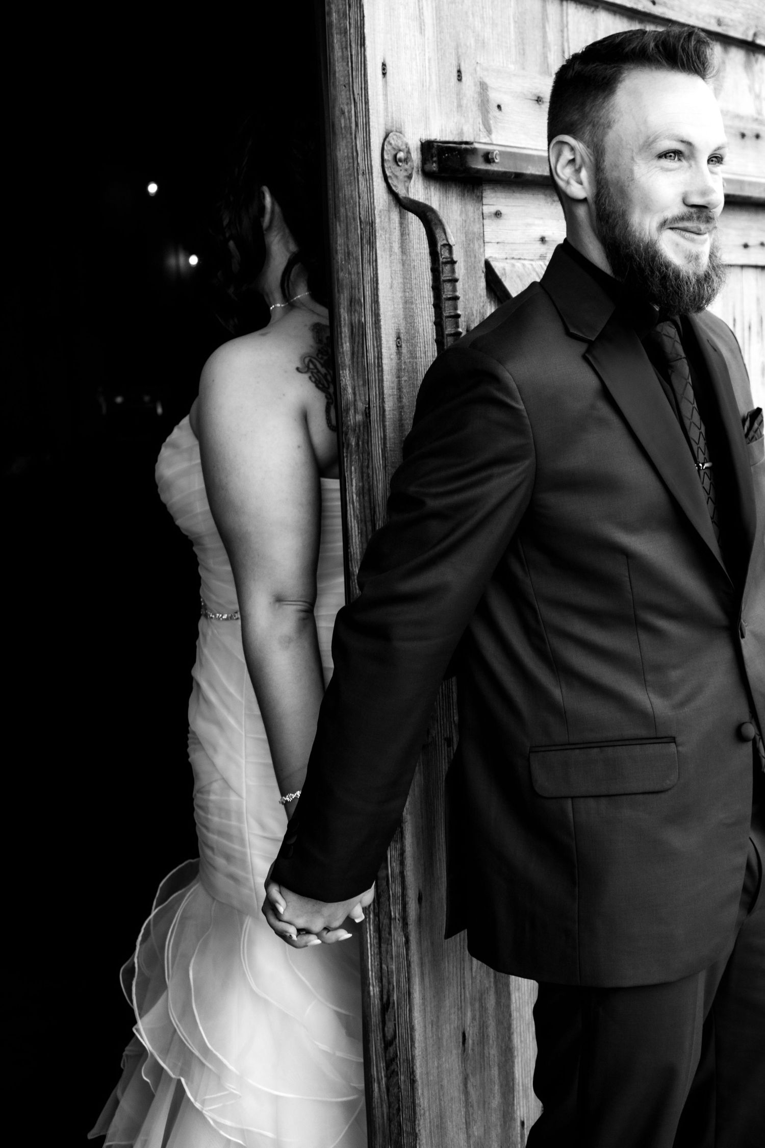 Artistic wedding photo showing couple in formal attire against rustic wooden wall.