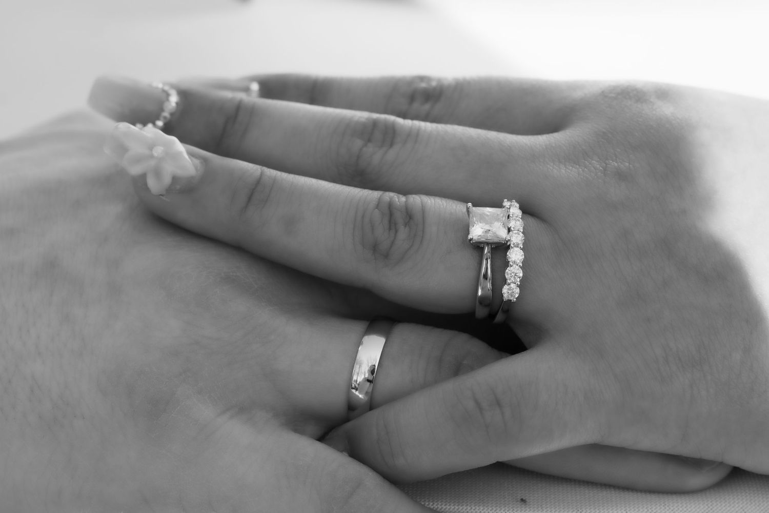Black and white close-up of wedding rings on intertwined hands.