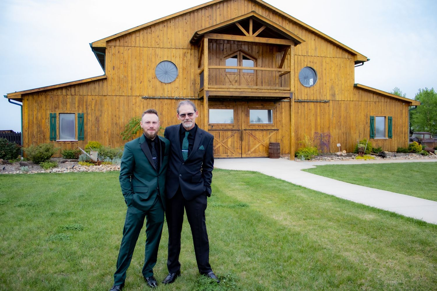A rustic wooden barn-style event venue with two circular windows and a covered porch entrance on a grassy lawn.