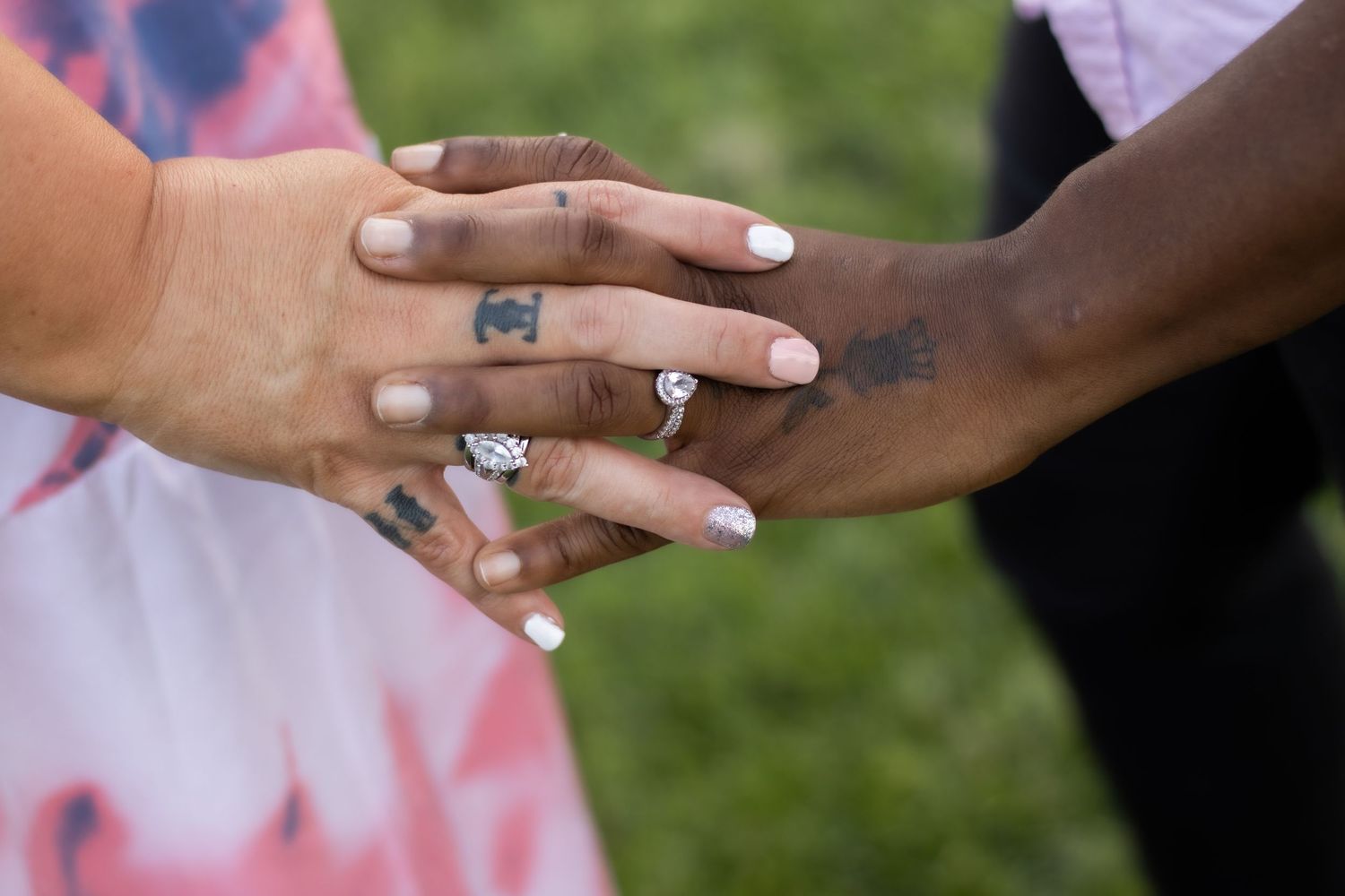 Close-up of hands with engagement rings touching in a tender moment against a green background.