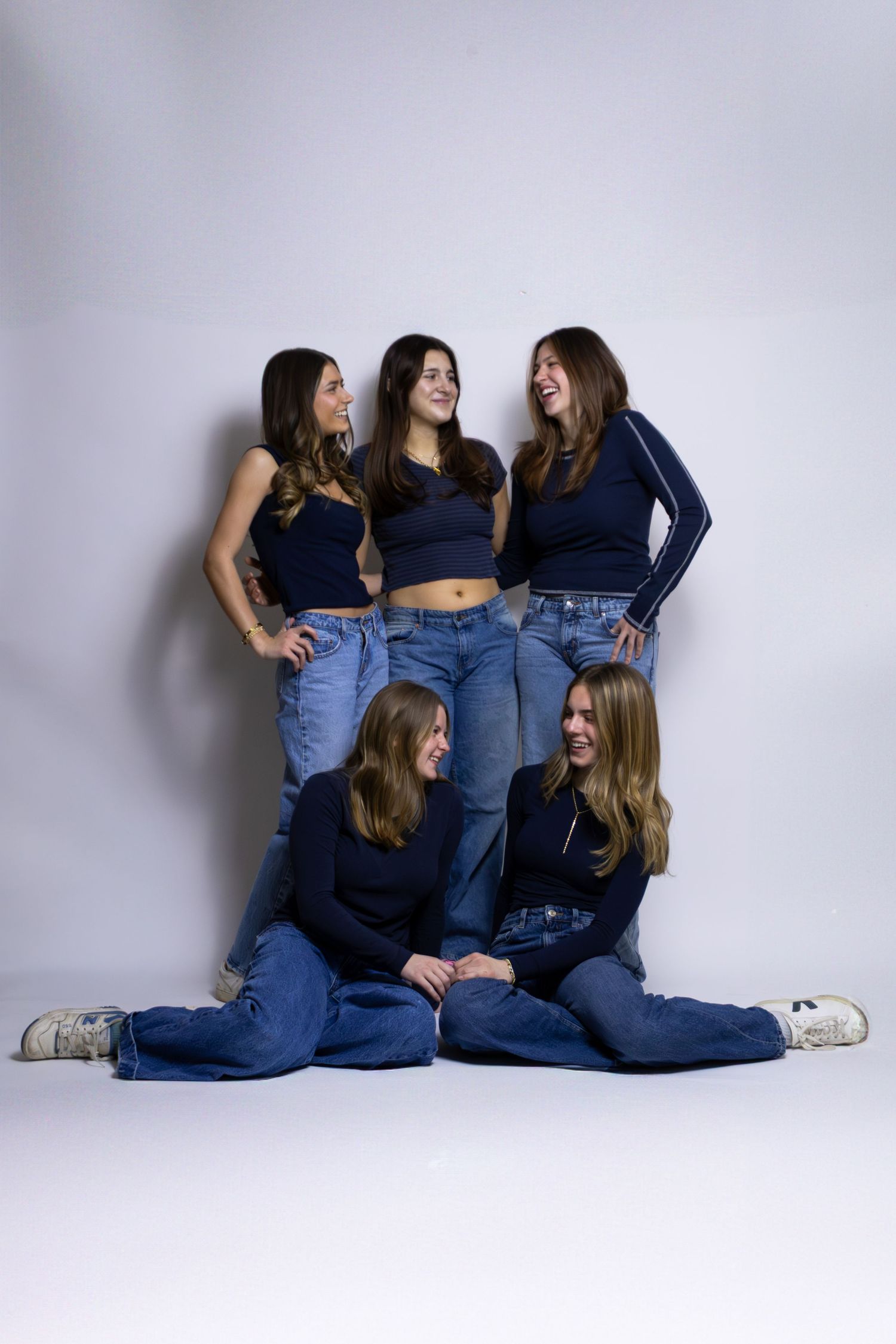 Group of five friends in matching navy tops and jeans pose together against white backdrop.