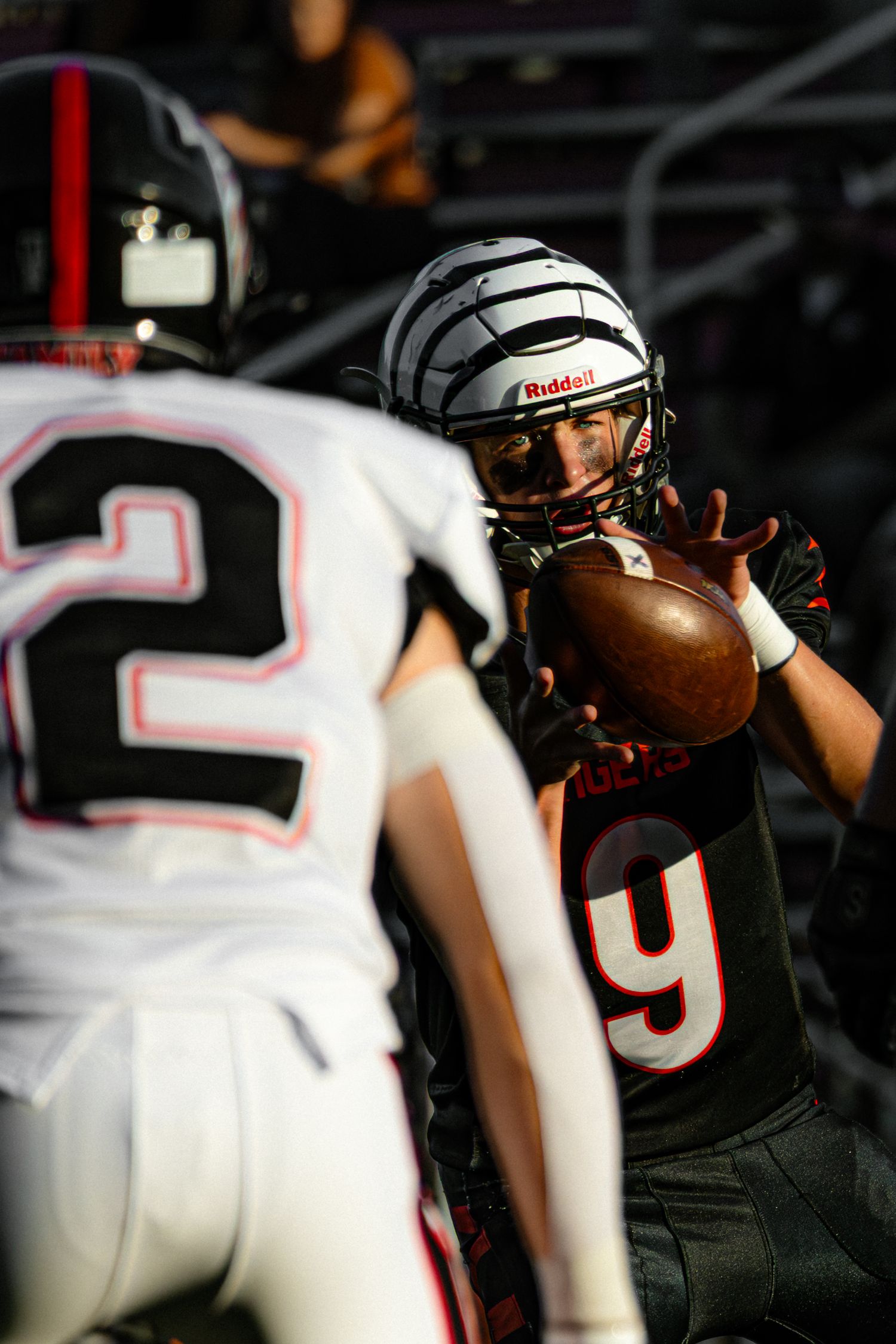 A football player in black uniform and striped helmet catches a pass while facing a defender in a white jersey.