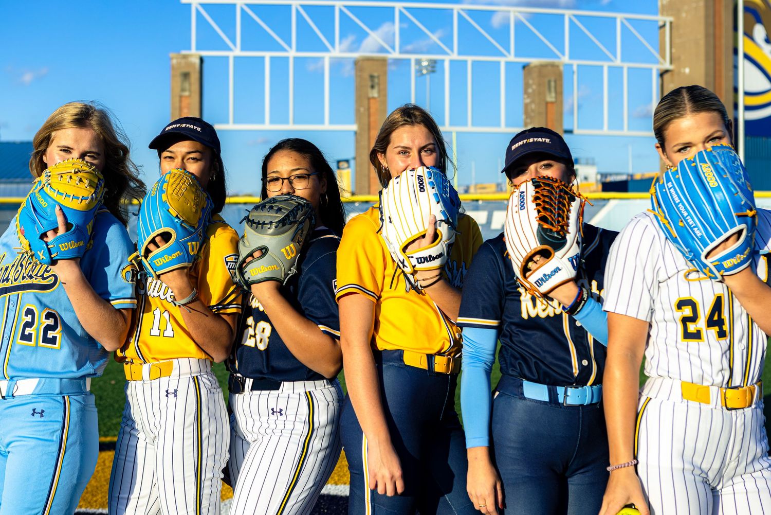 Baseball team members wearing light blue and yellow uniforms pose together for a group photo on the field.