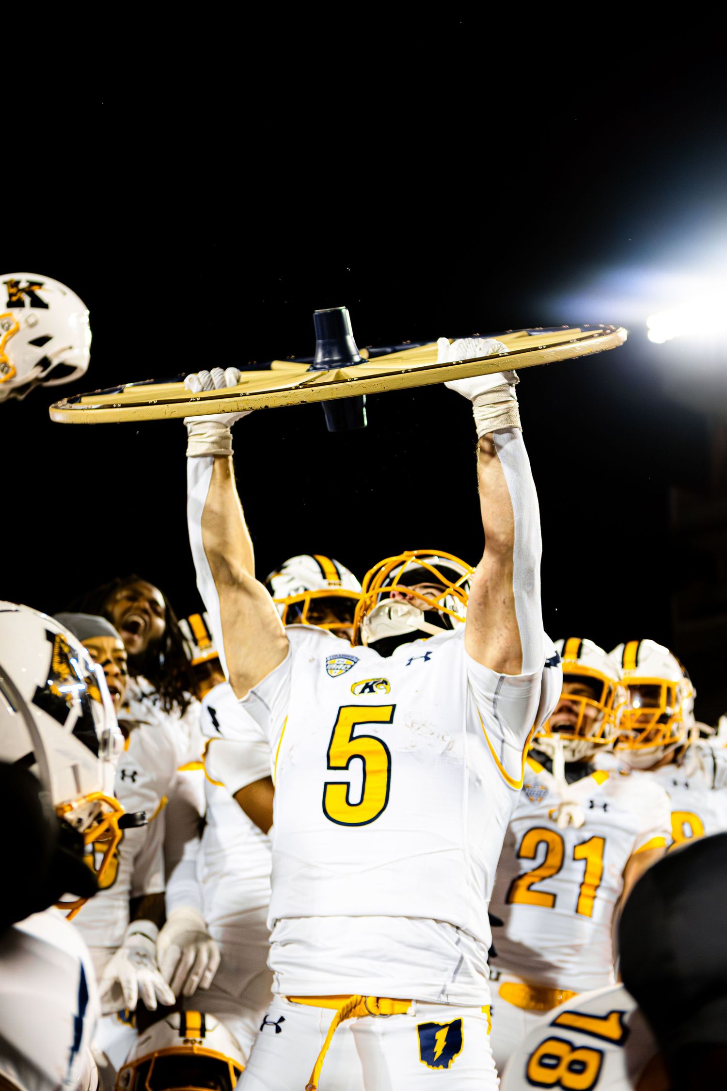 Football players in white and gold uniforms hold up their helmets in celebration after a victory.