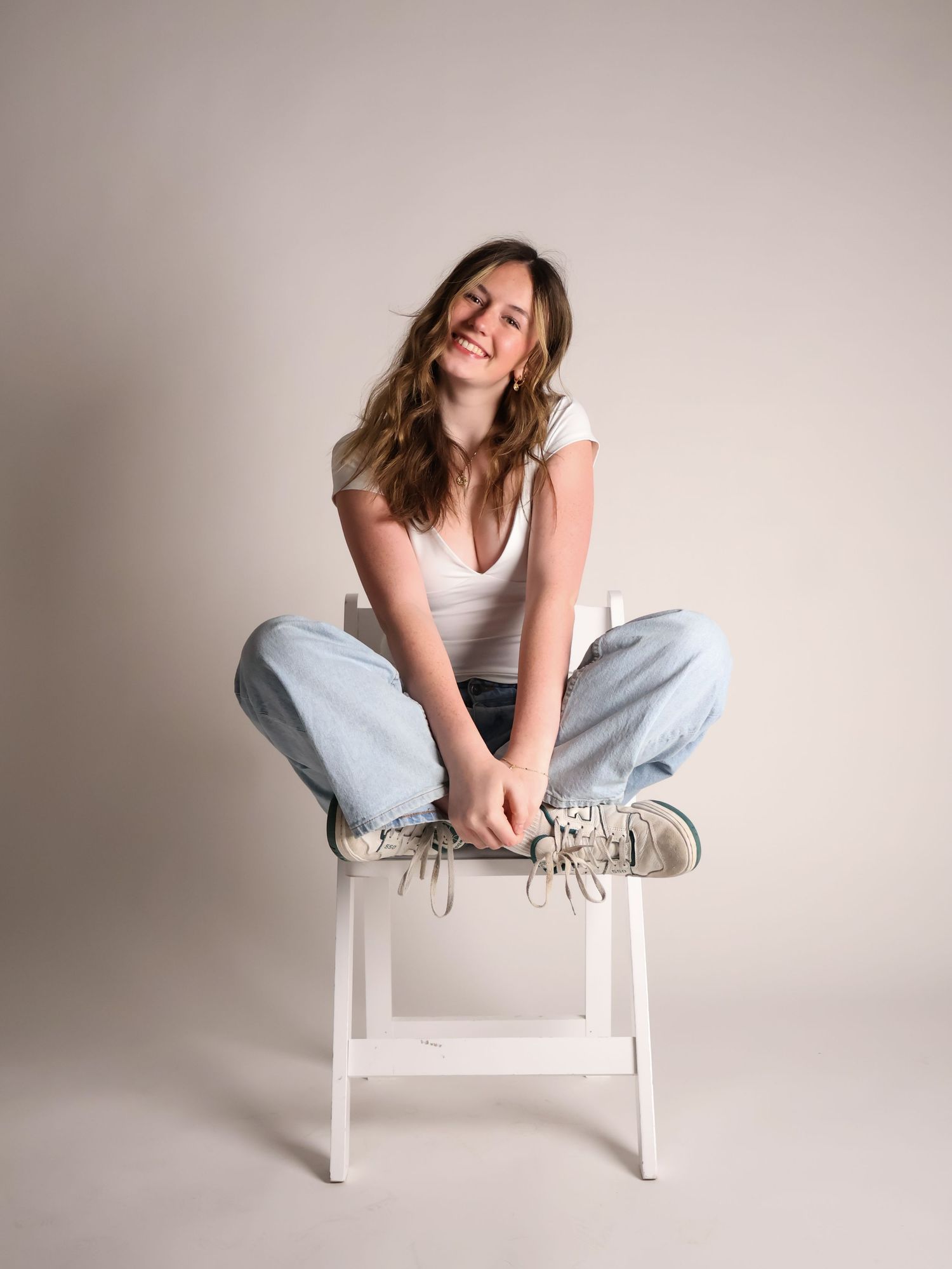 Portrait photo sequence of someone in a white tank top and jeans seated casually on a white chair against neutral background.