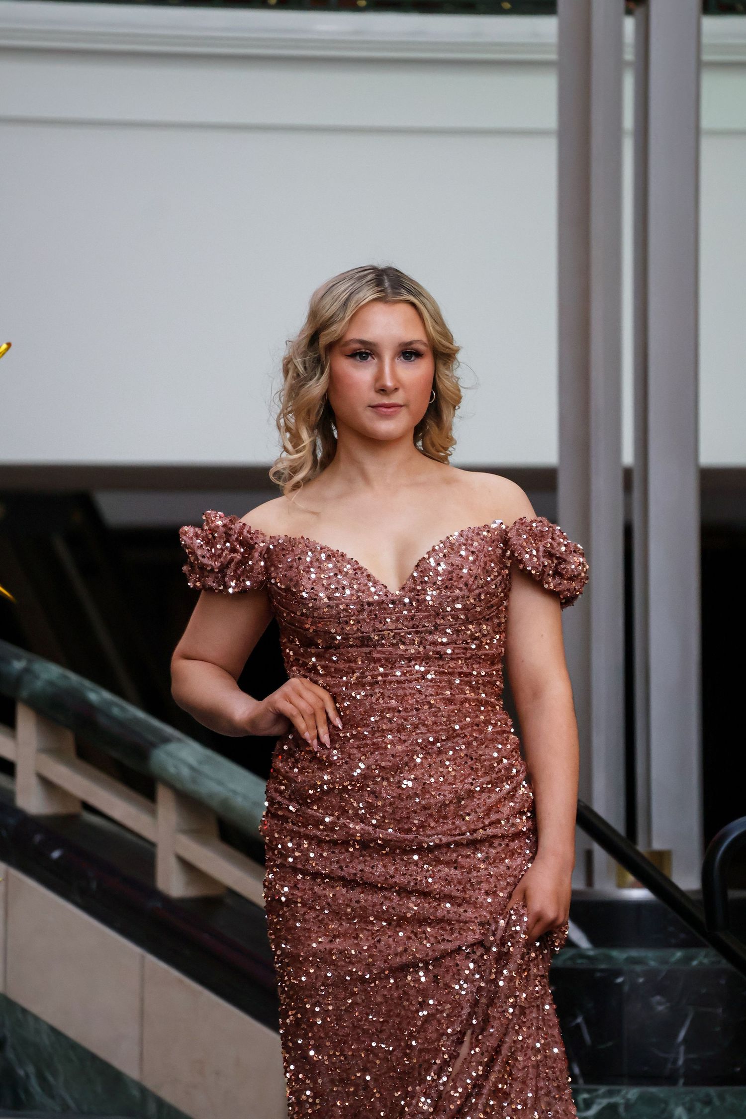 A flowing rose gold sequined evening gown with sweetheart neckline and off-shoulder sleeves.