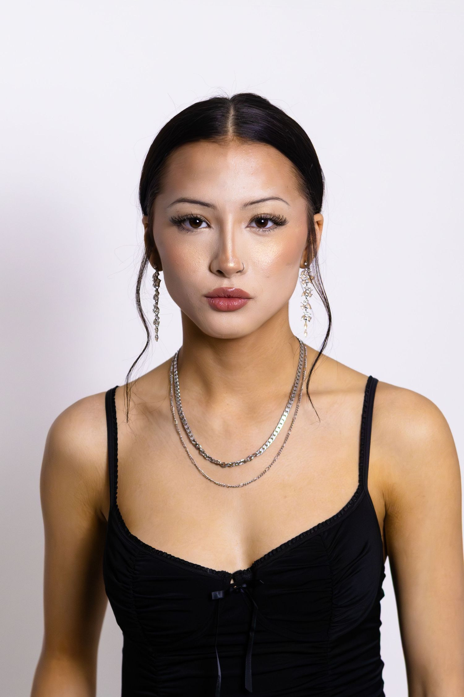 Elegant model wearing a black slip dress and layered silver necklaces against a white studio background.