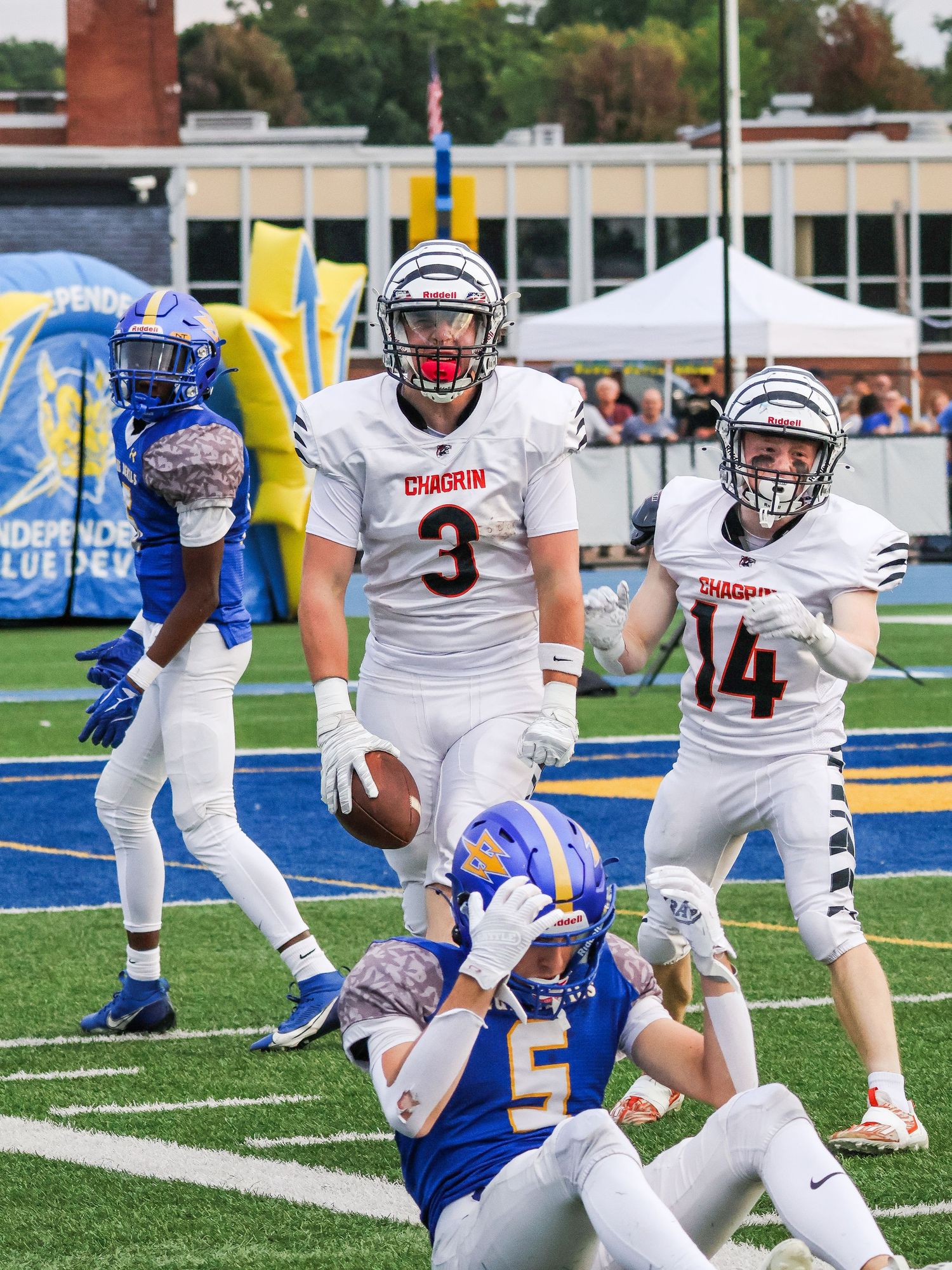 Football players from opposing teams clash during a play on a blue turf field.