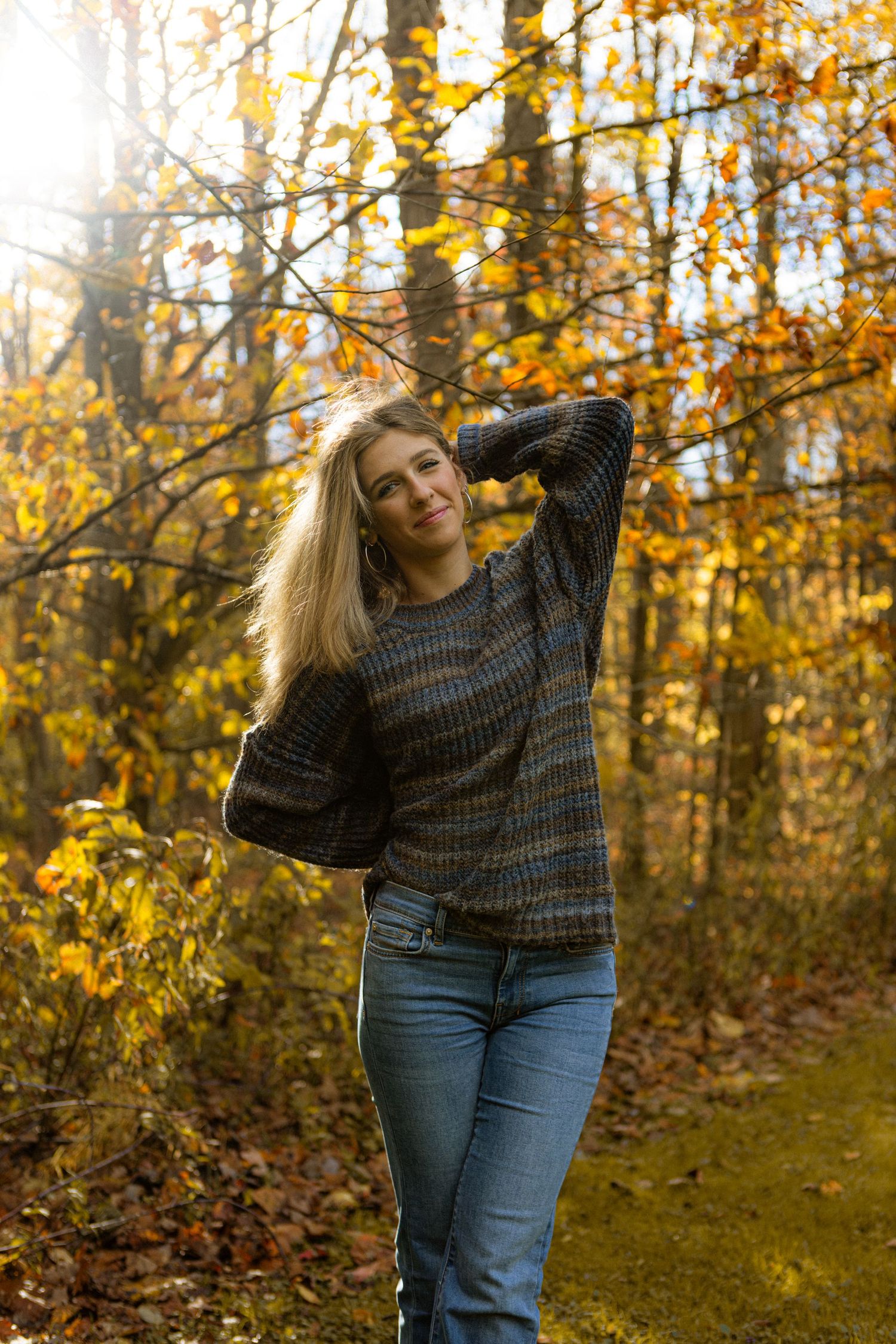 Person in a cozy sweater poses in a sunlit autumn forest with golden leaves and warm lighting.