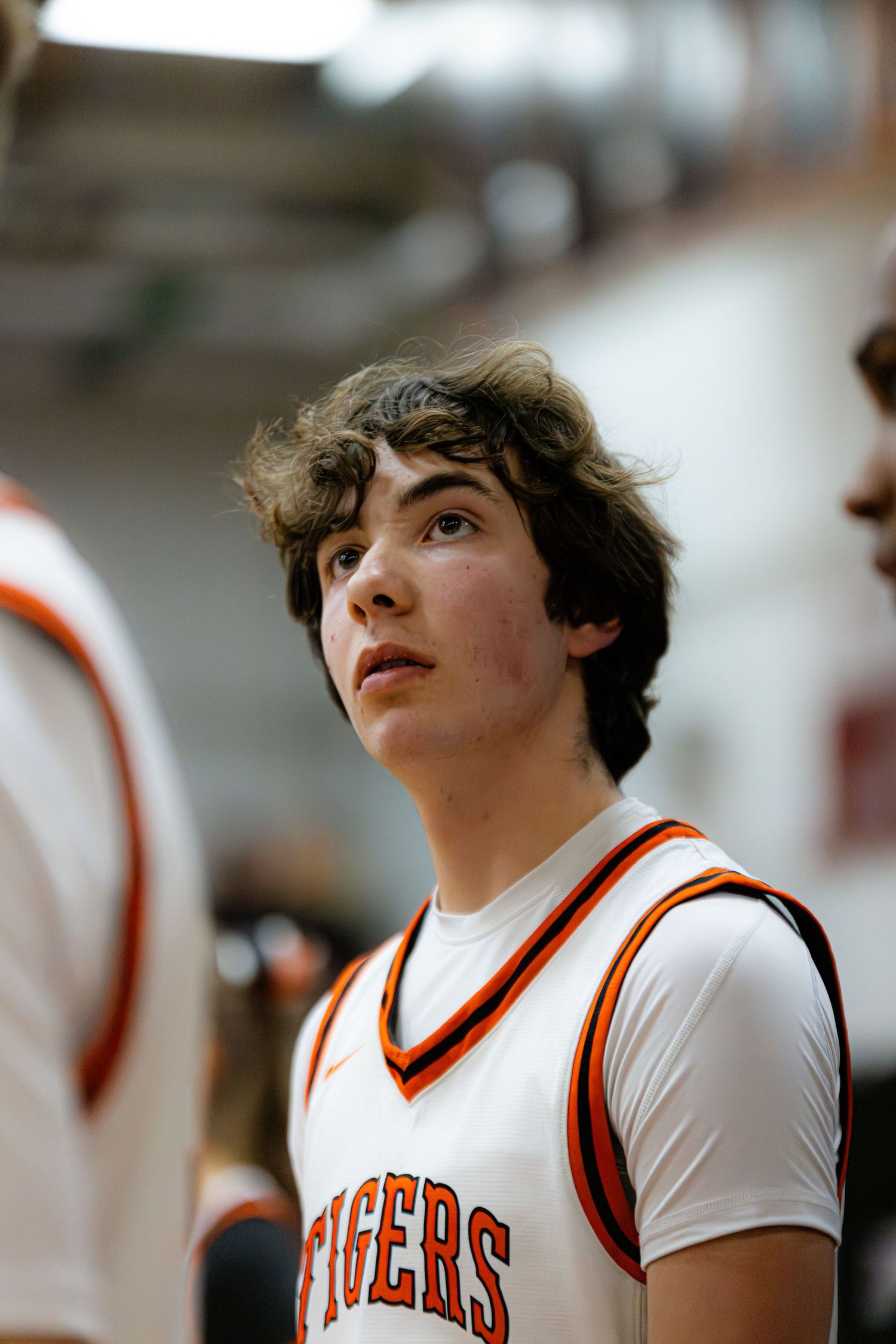 A student athlete in a white and orange Tigers basketball jersey looks upward during a game.