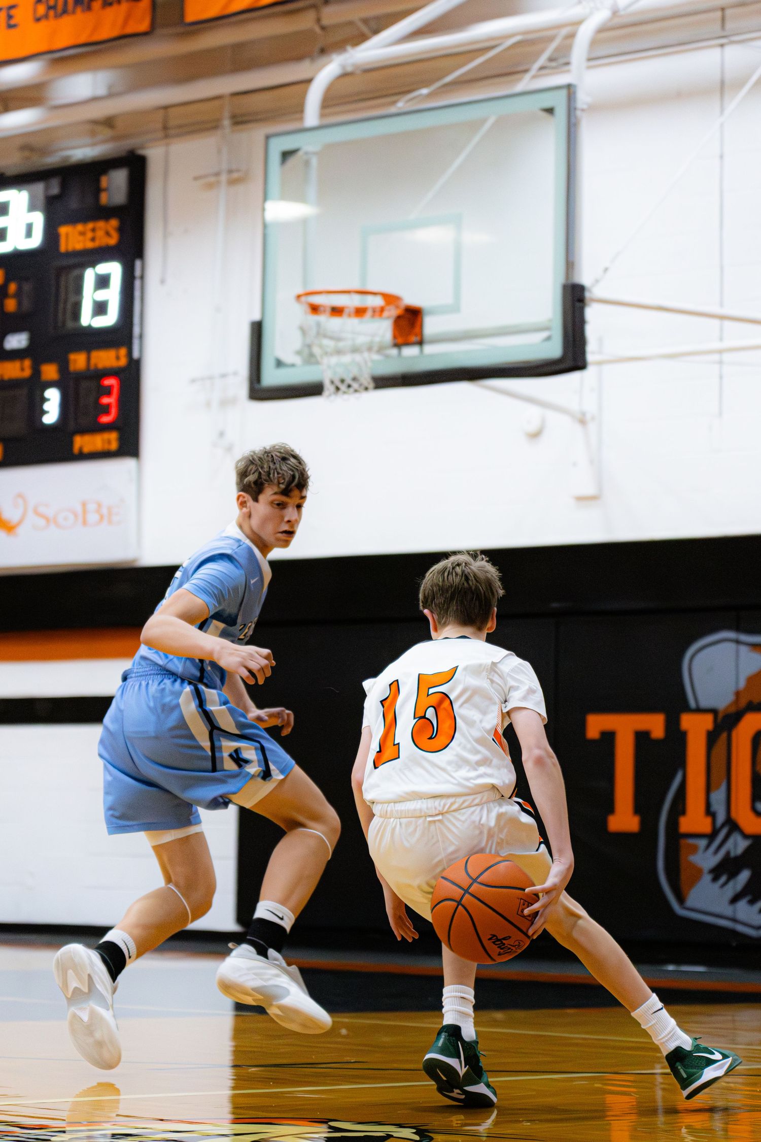 Basketball players compete on indoor court during game showing sequence of dribbling and defensive moves.