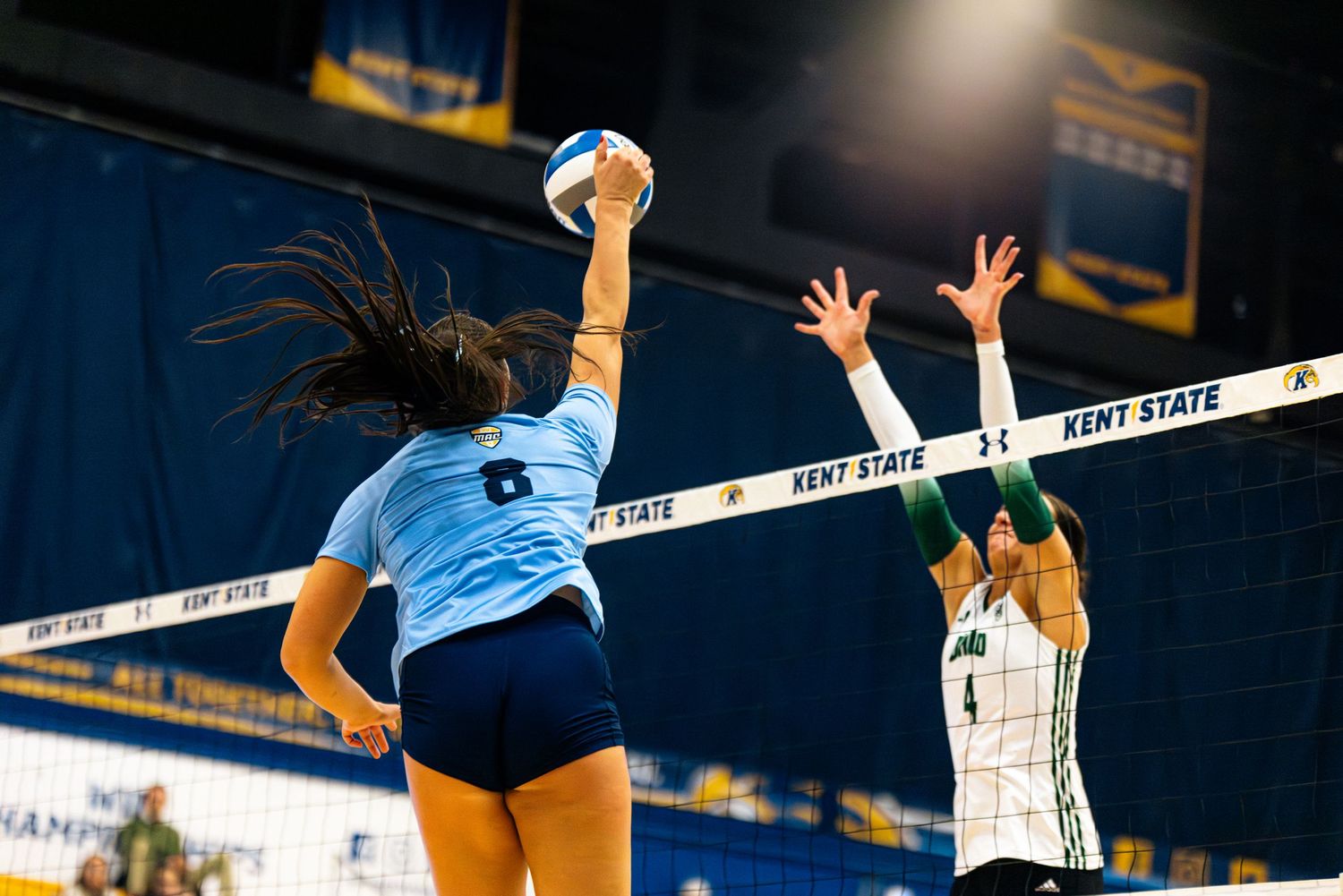 Volleyball players leap at the net during an intense match as they compete for a crucial point.