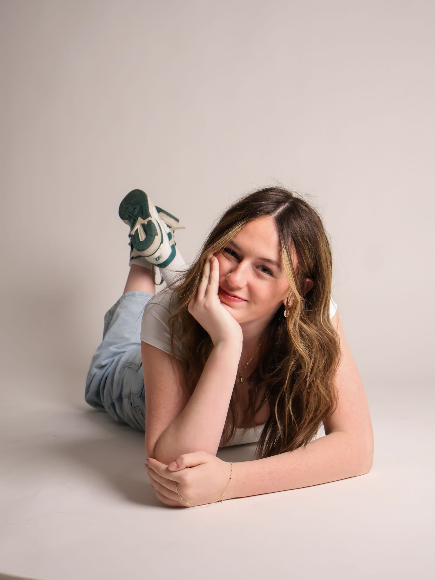 A person in denim overalls lies on the floor in a relaxed pose against a neutral background, wearing stylish sneakers.