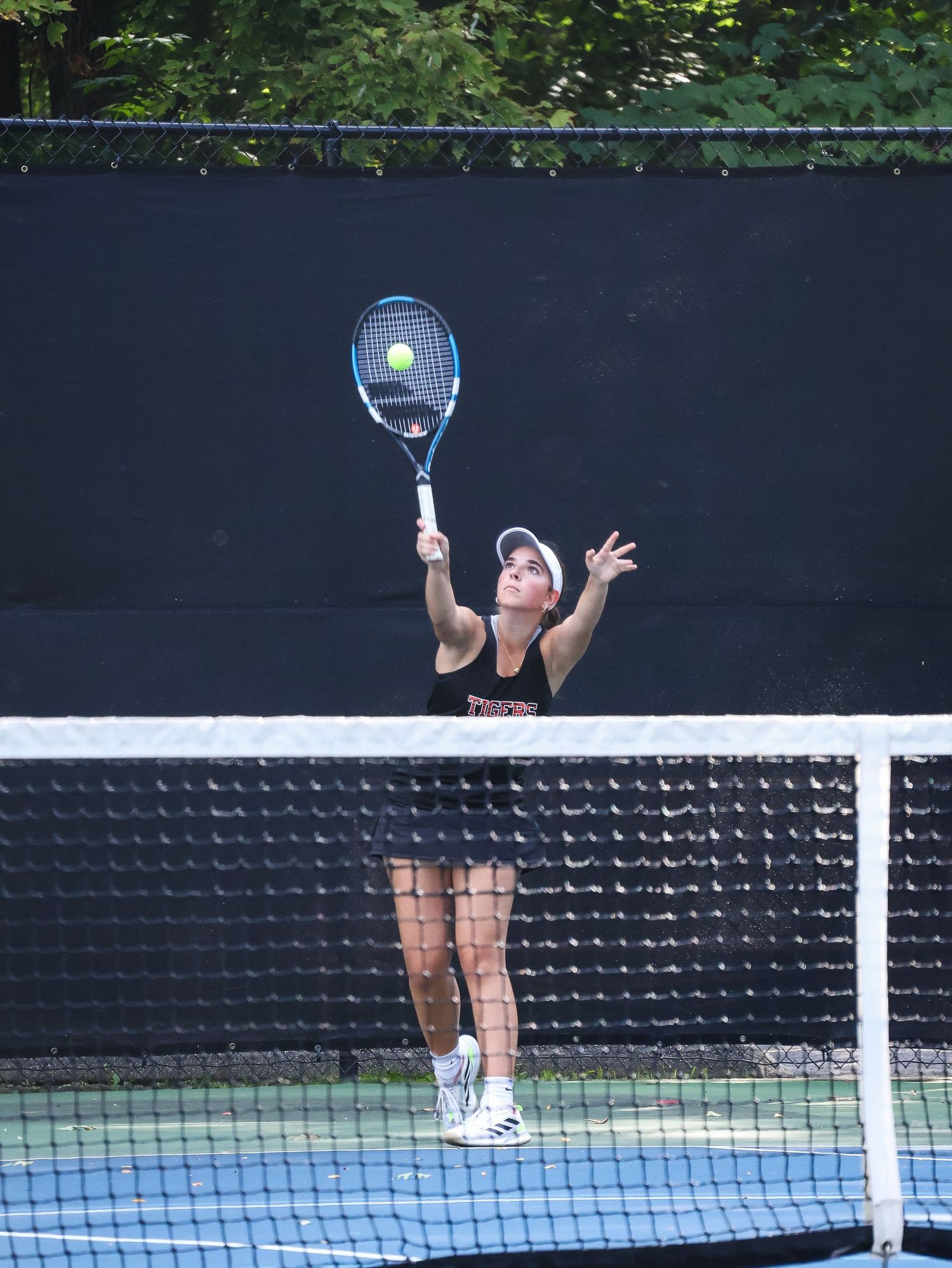 Tennis player reaching up to serve the ball during match on outdoor court.