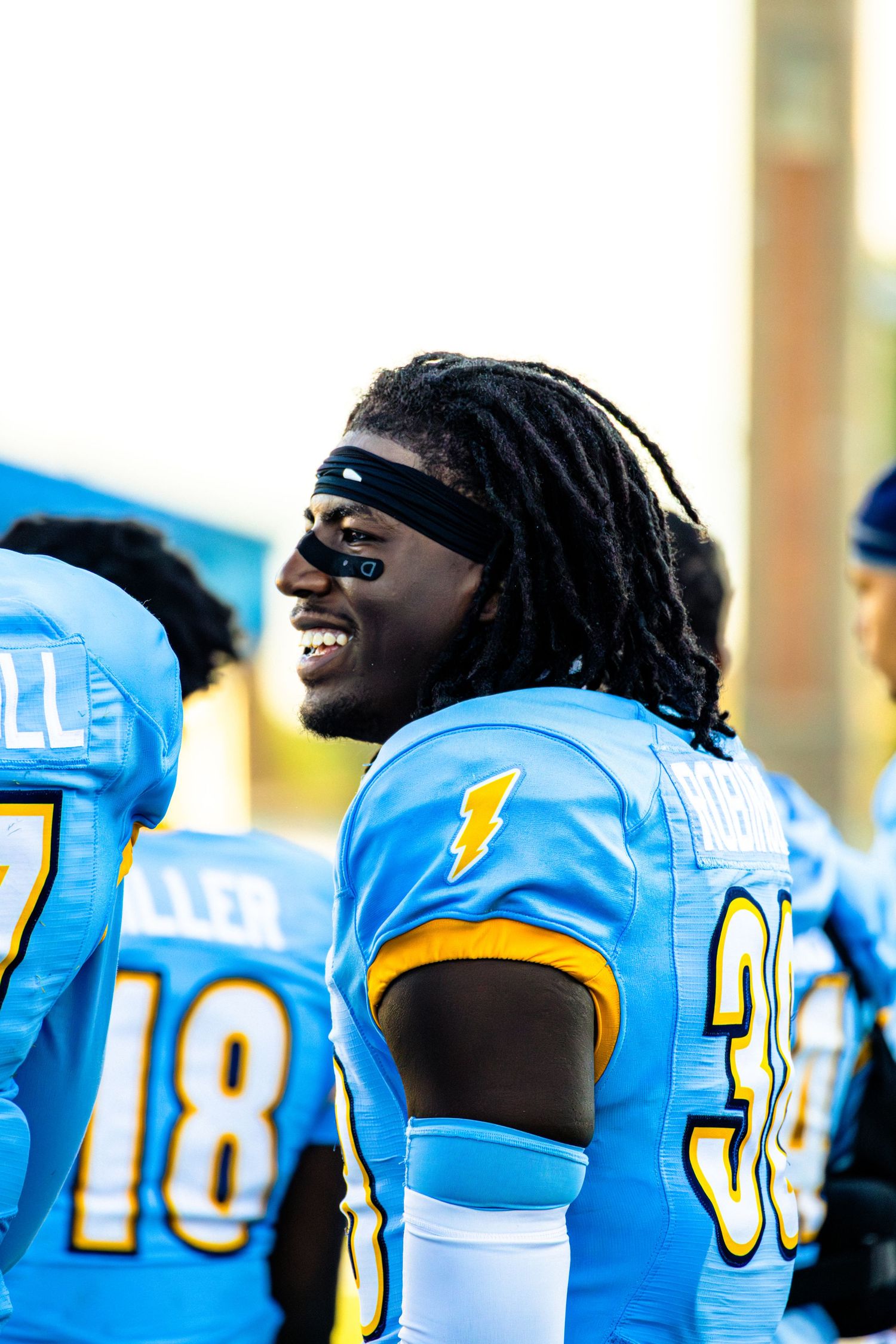 Football players in light blue and yellow uniforms laughing and celebrating on the sidelines during a game.