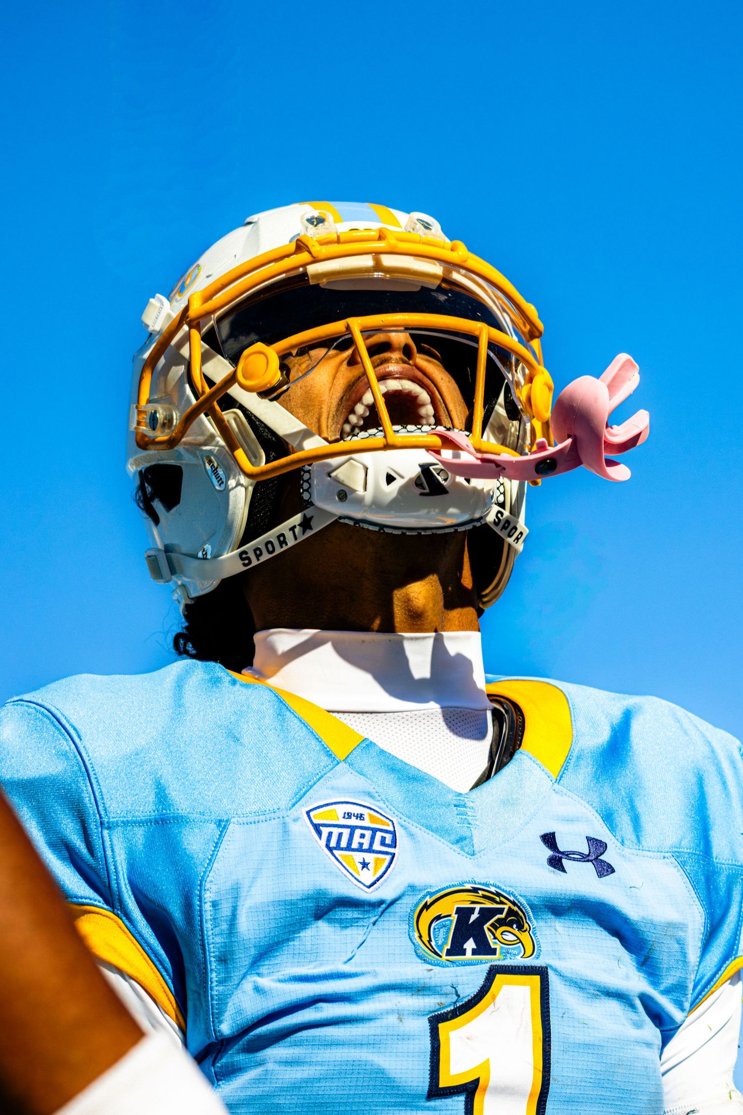 Close-up view of gold-tinted football helmet visors reflecting bright blue sky on a sunny day.