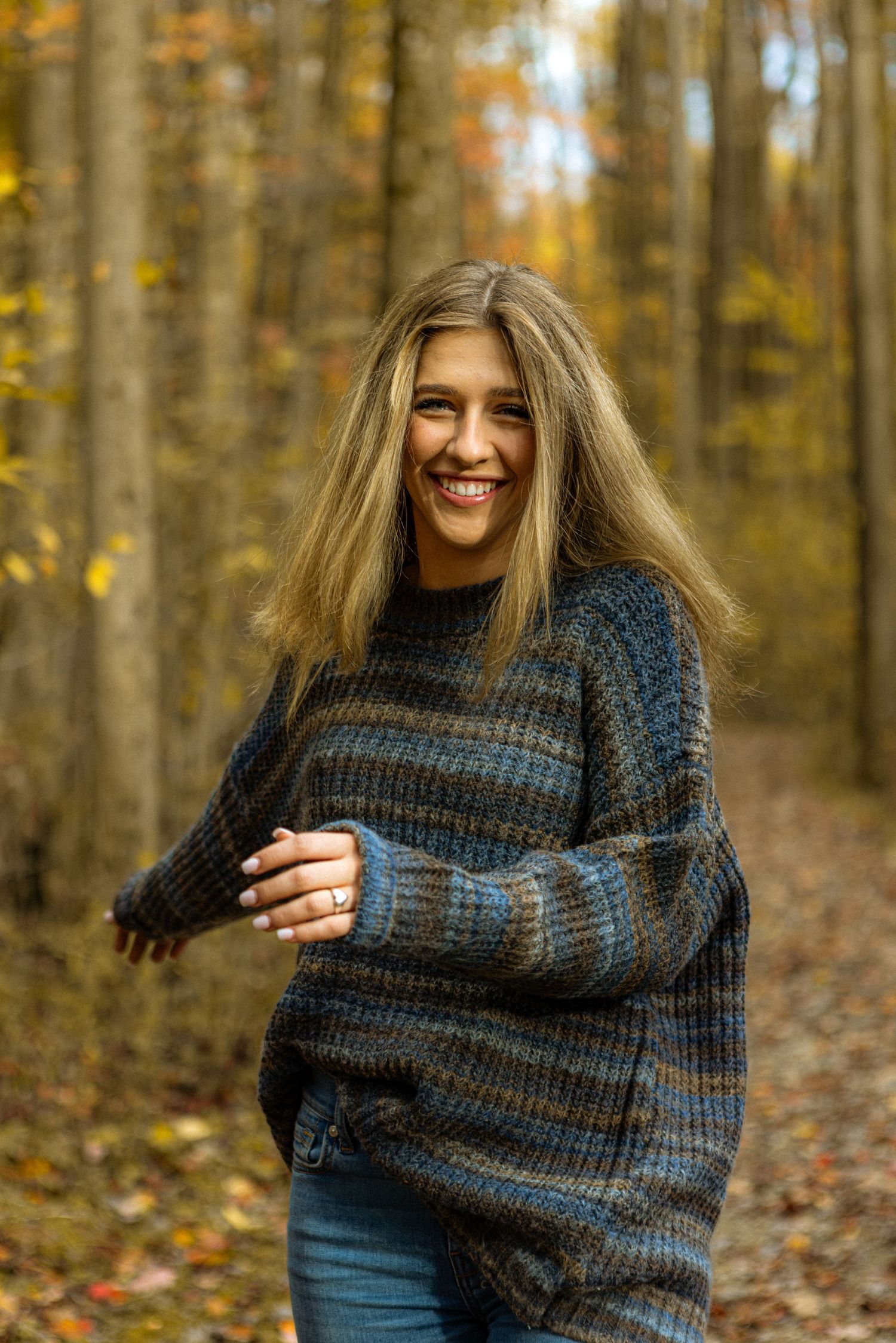 A person wearing a striped sweater laughs joyfully while standing in an autumn forest with golden leaves.