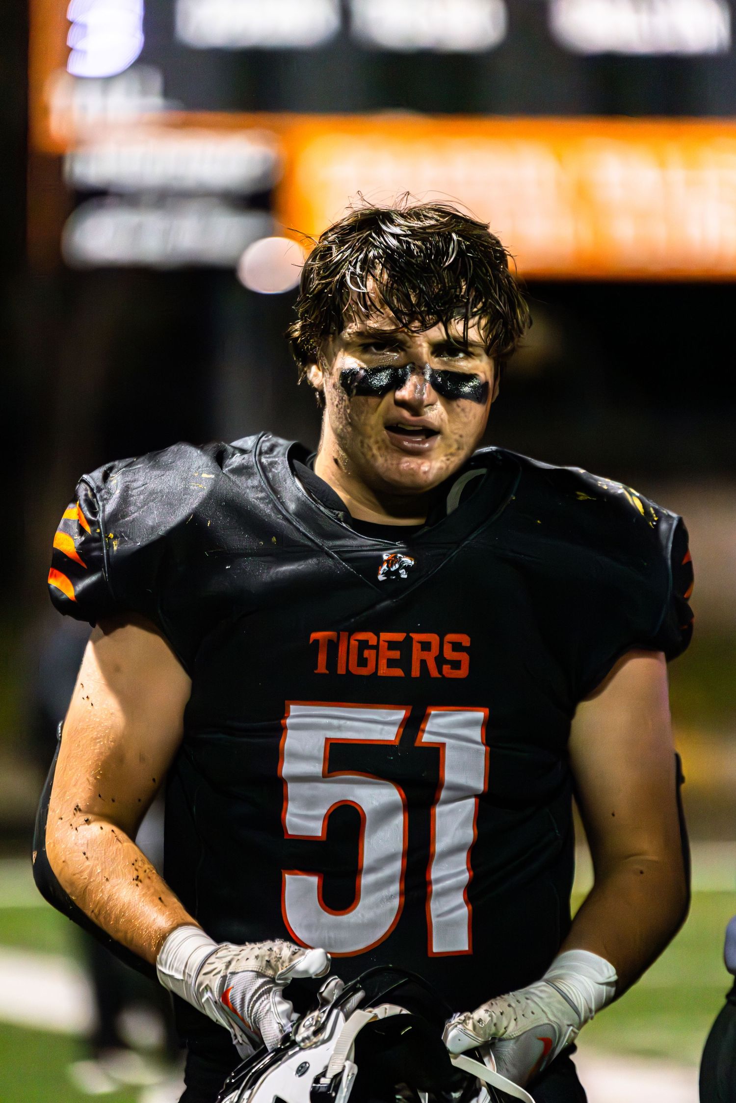 High school football players in black Tigers jerseys with orange lettering stand together on the field during a game.