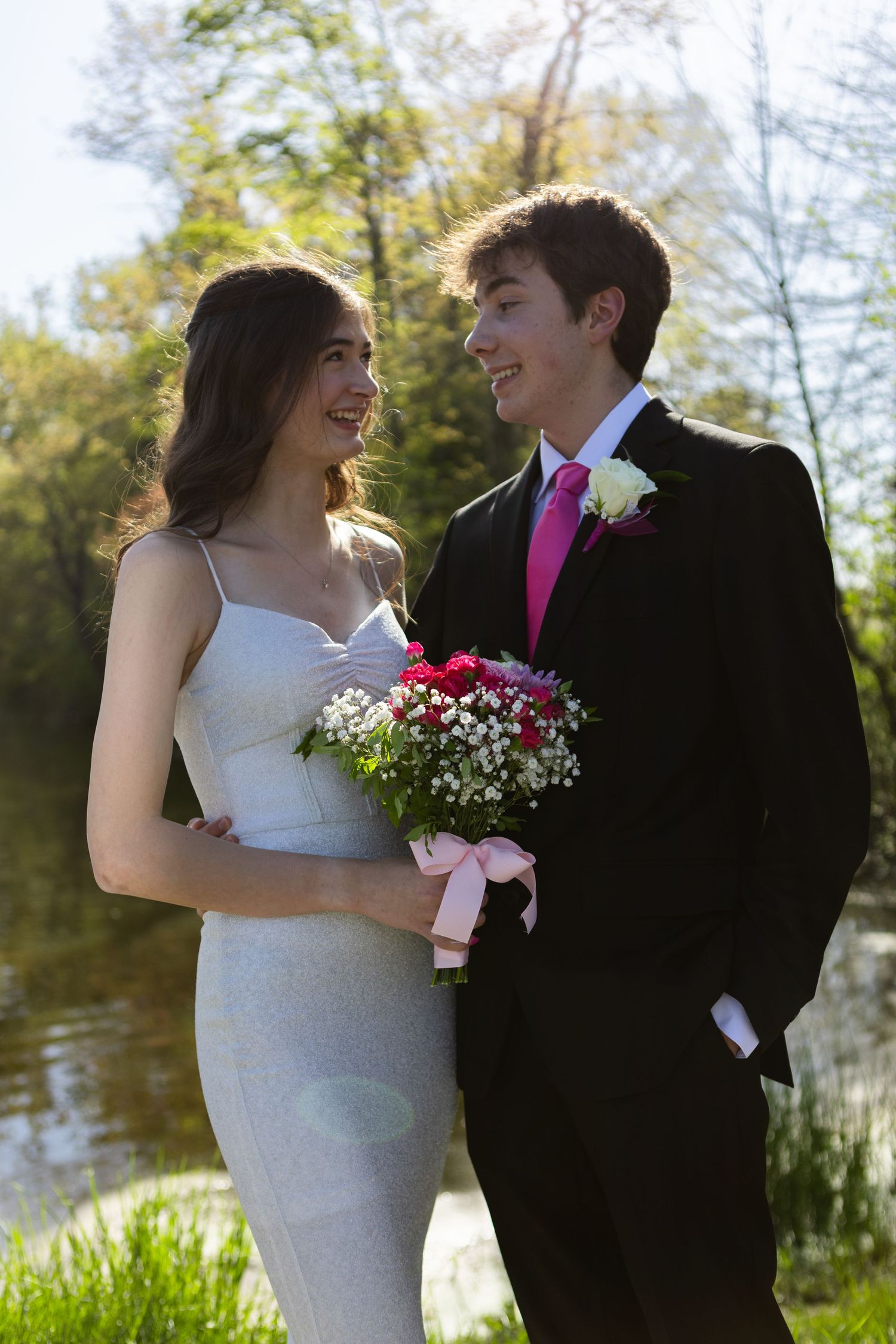 Joyful wedding couple laughing together by waterside in formal attire.