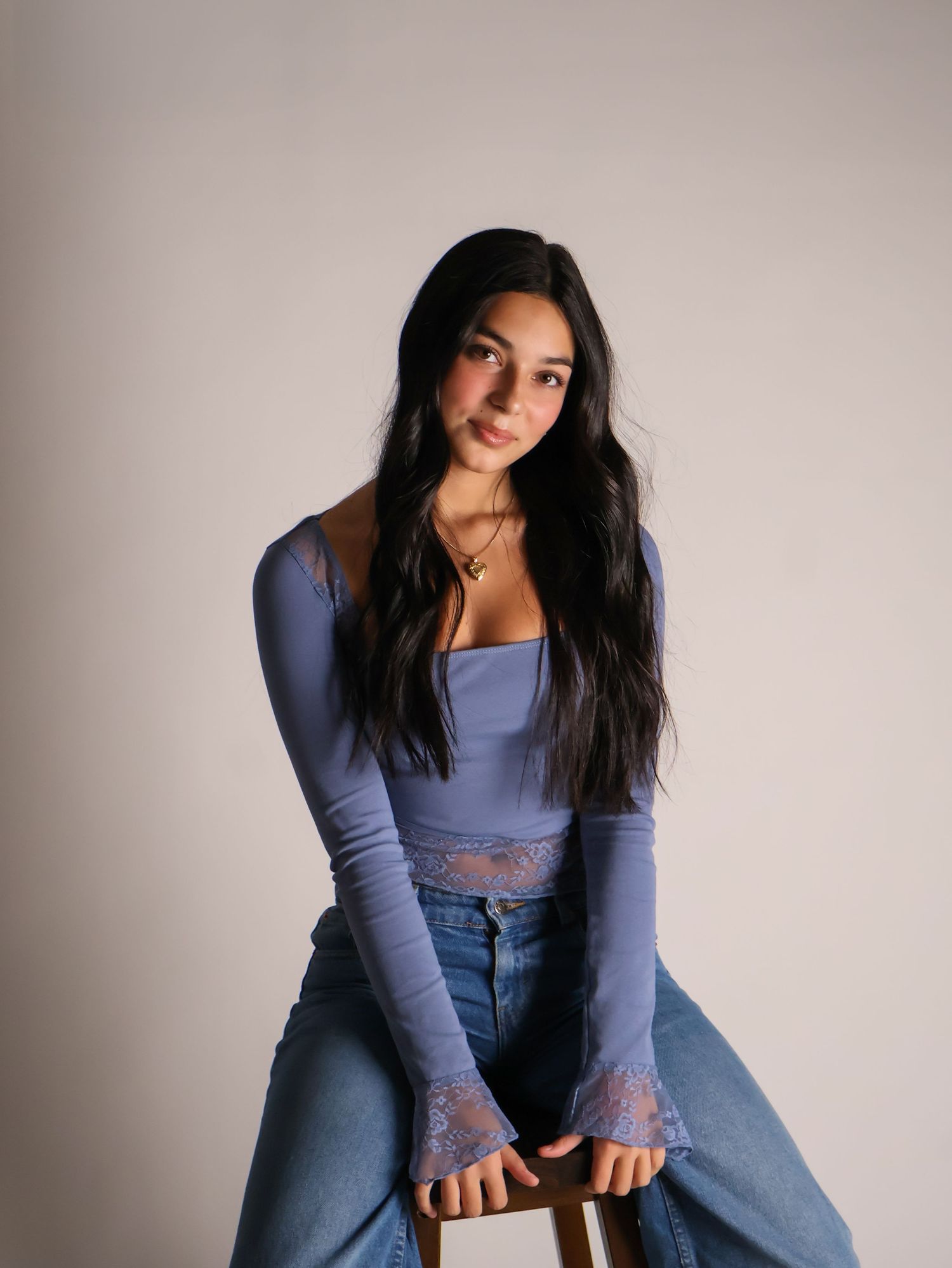 Portrait shot in studio lighting features subject in lavender long-sleeve crop top and high-waisted jeans against neutral background.