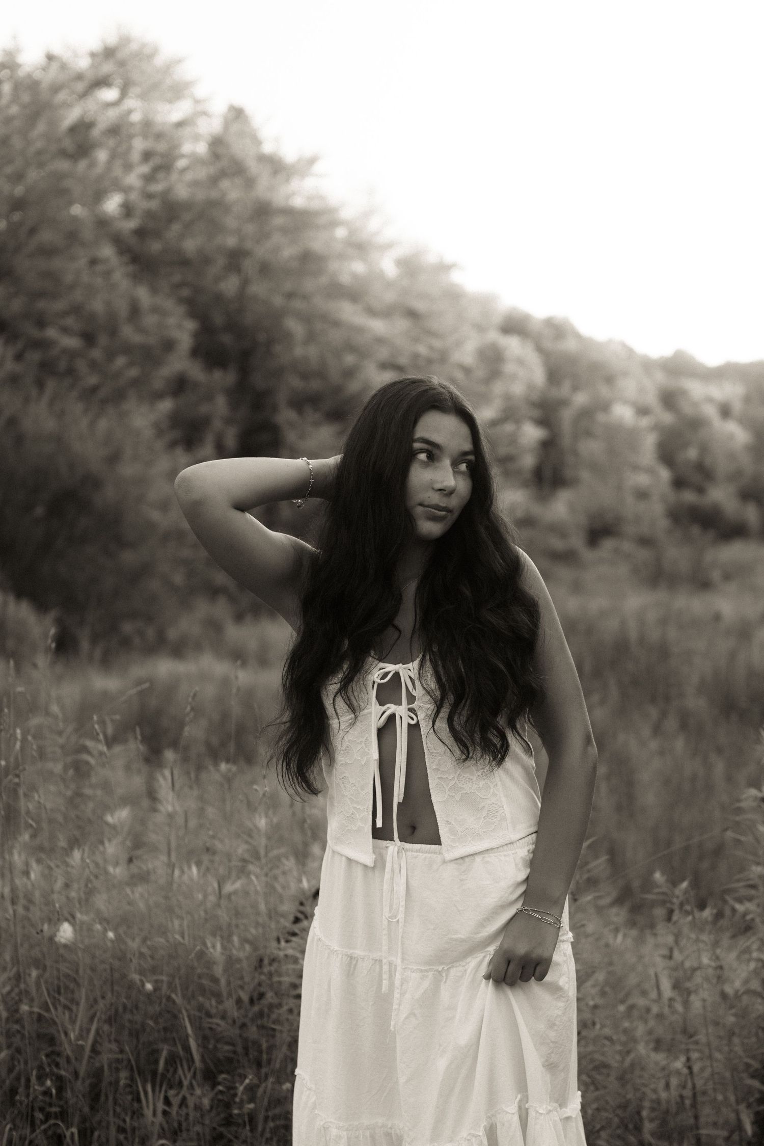 A person in a white dress stands in a meadow with expressive poses in a series of dreamy black and white photographs.